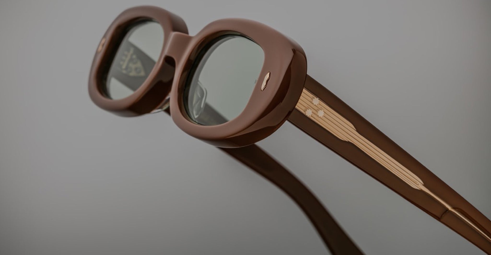 Close-up of Jacques Marie Mage Besset sunglasses, brown oval frames, tinted lenses, gold detailing, front angle.
