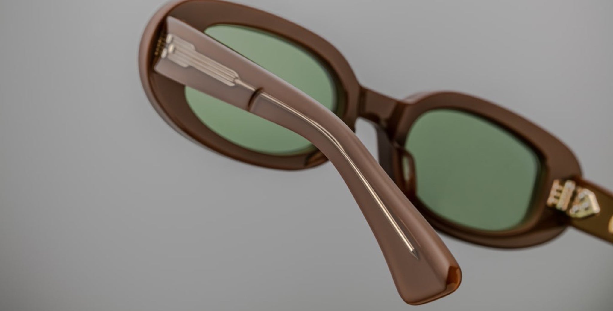 Close-up of Jacques Marie Mage Besset sunglasses, brown frame with green lenses, side arm and hinge visible from a side angle.