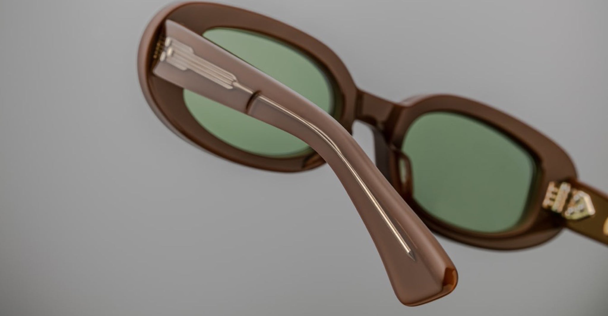 Close-up of Jacques Marie Mage Besset sunglasses, brown frame with green lenses, side arm and hinge visible from a side angle.