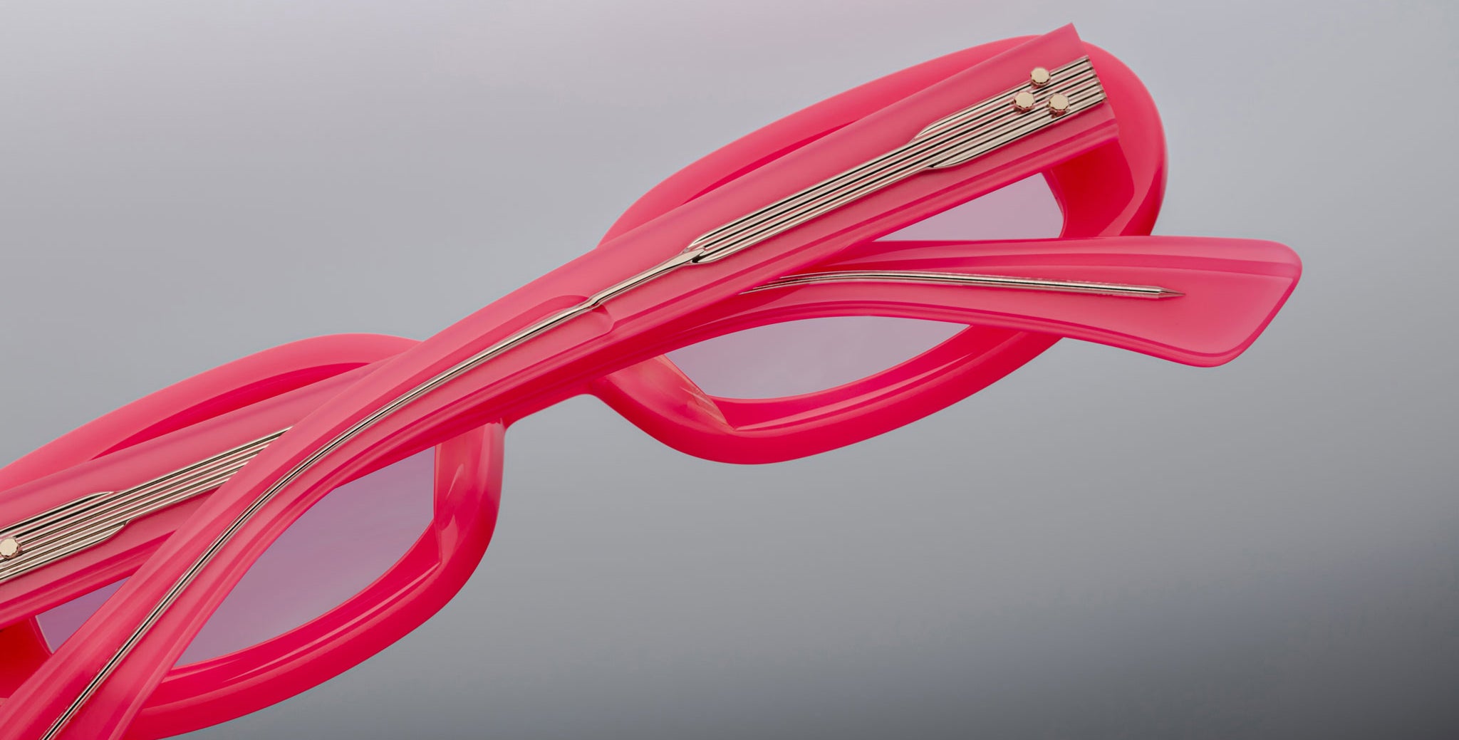 A close-up of two Jacques Marie Mage Besset eyeglasses in bright pink with metallic temple accents, stacked atop each other against a plain gray background.