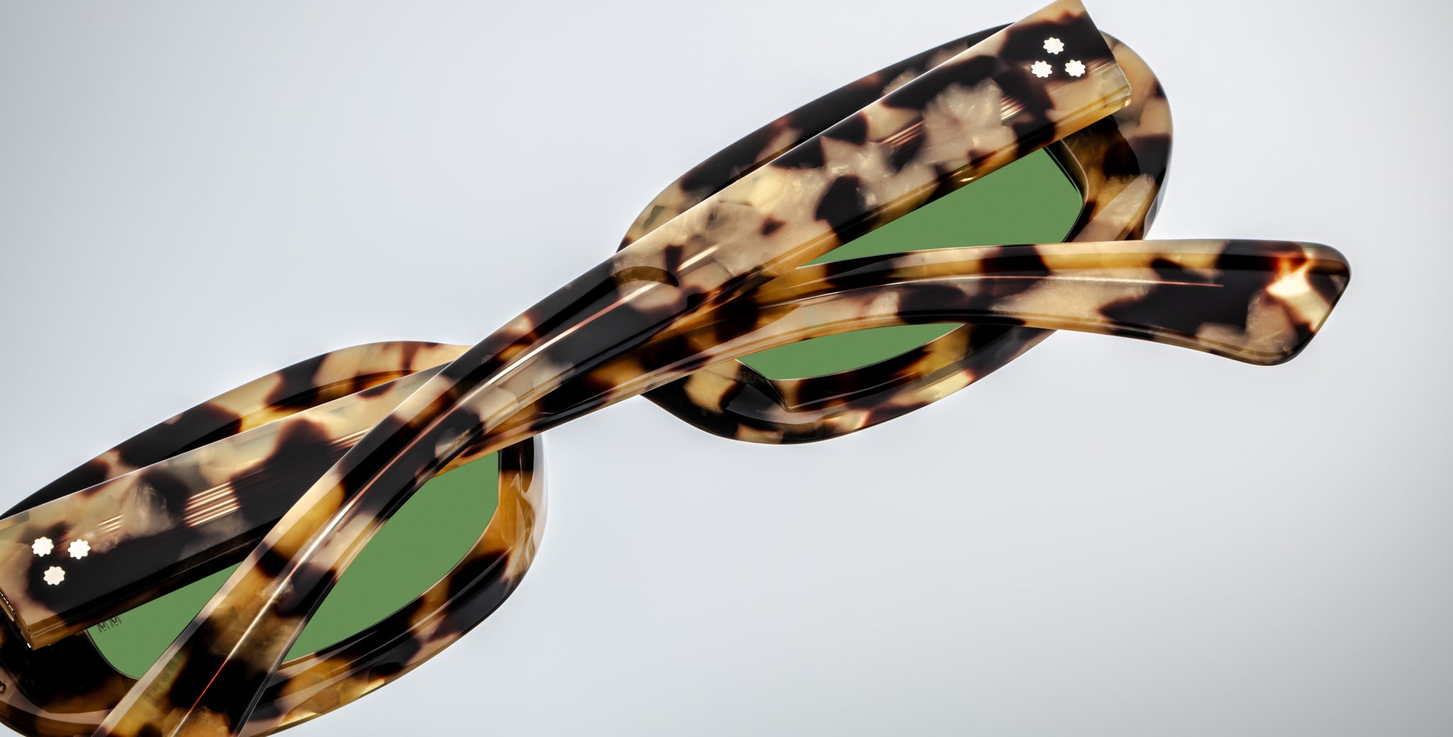 Close-up of Jacques Marie Mage Besset sunglasses, featuring tortoiseshell frames, green lenses, and bold temples.