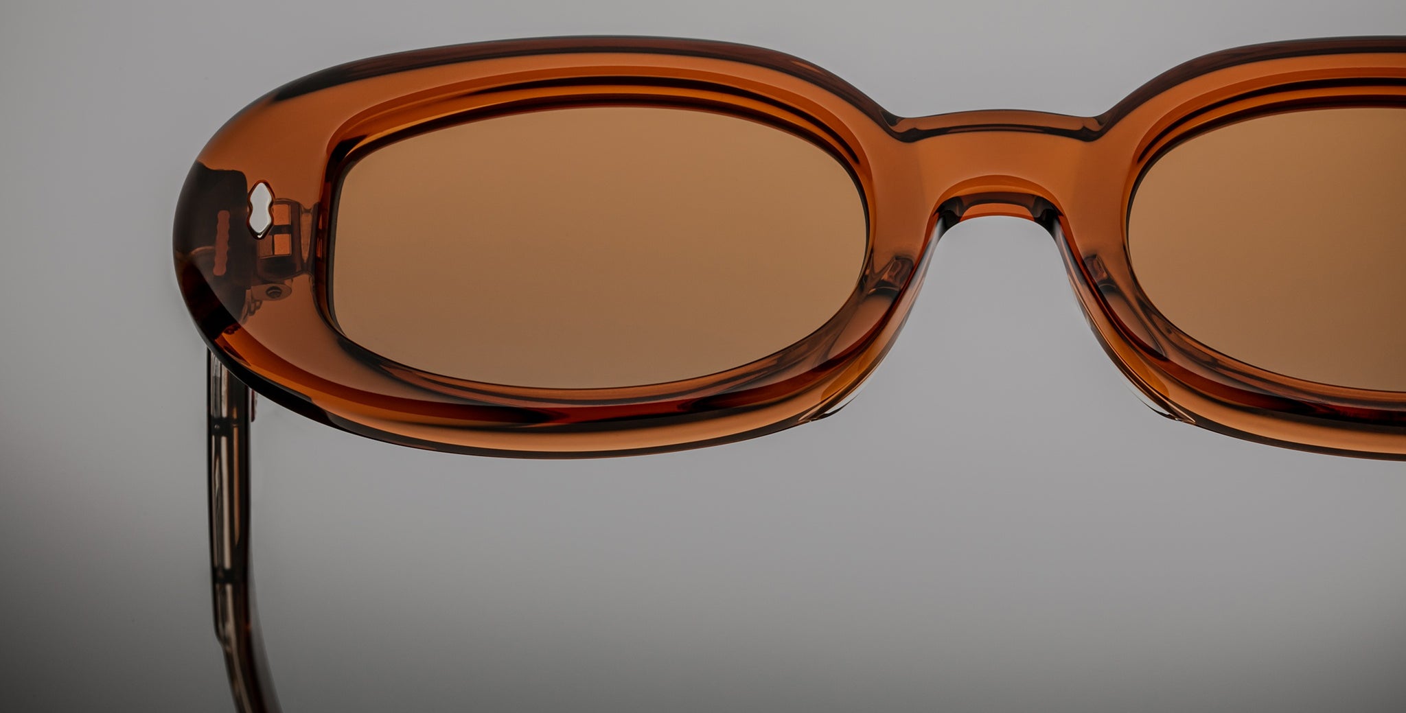 Close-up of Jacques Marie Mage Besset sunglasses, brown oval lenses with transparent frames, photographed from the front.