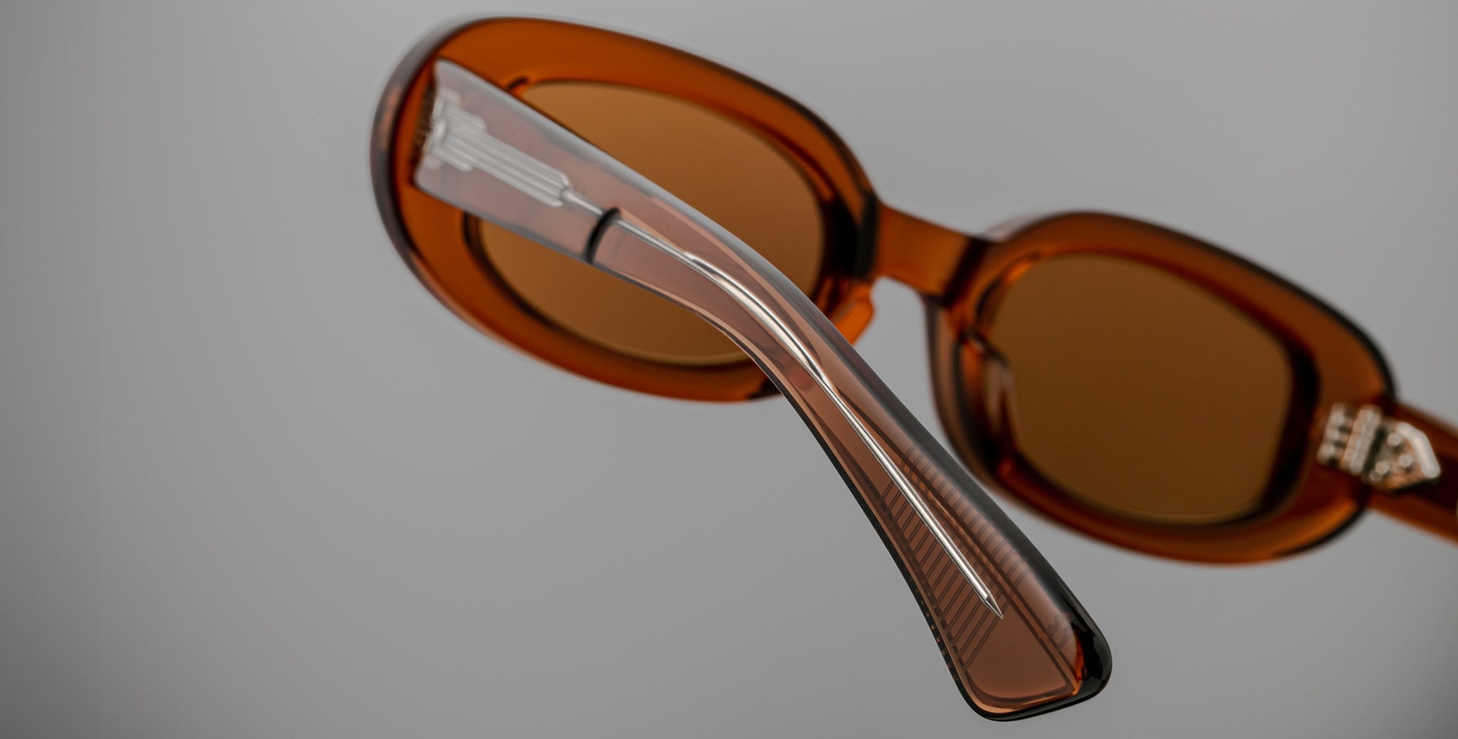 Close-up of Jacques Marie Mage Besset brown oval sunglasses with translucent acetate arms, angled to show frame details.