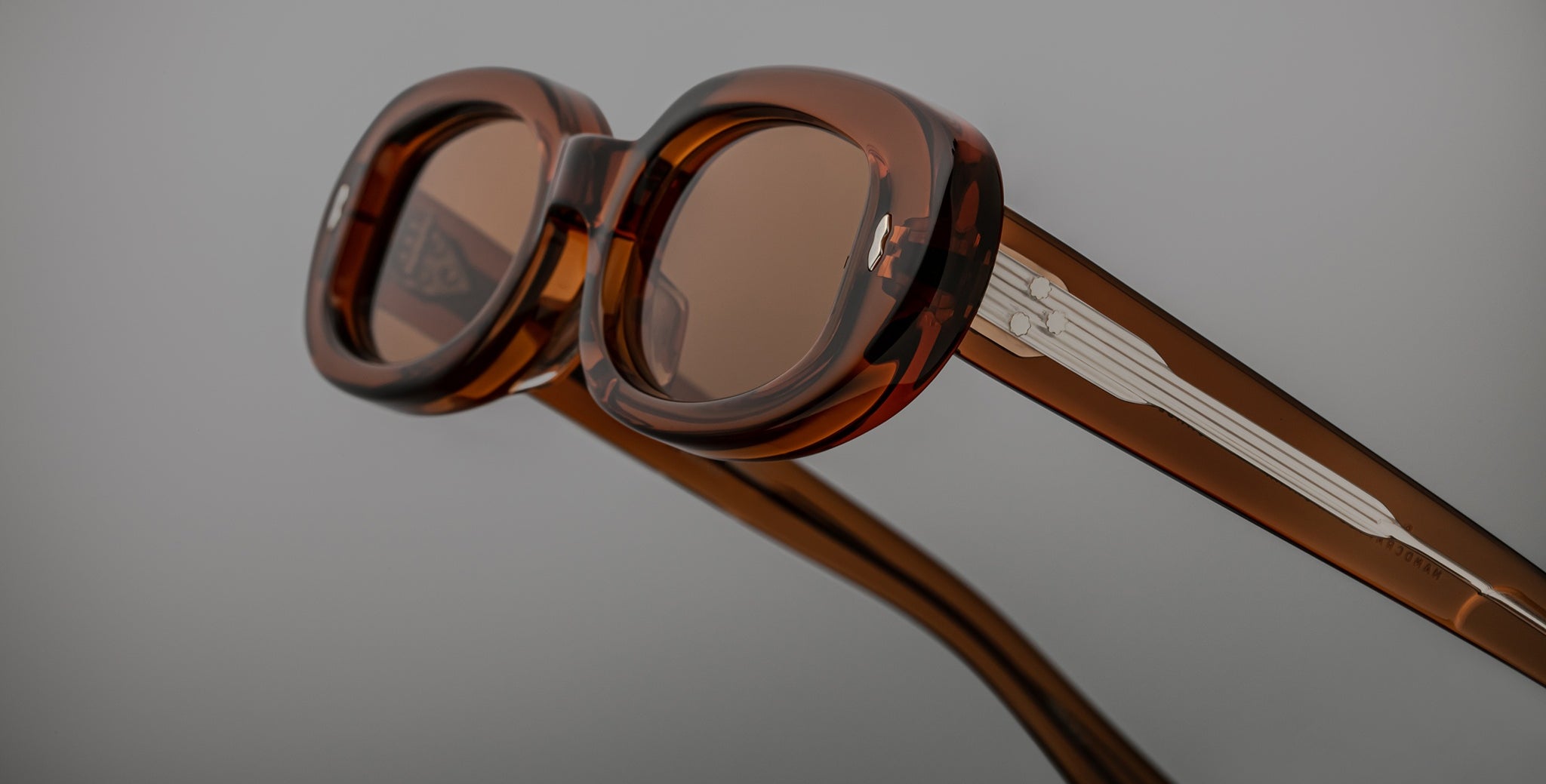 Close-up of Jacques Marie Mage Besset sunglasses, featuring brown translucent retro round frames and silver accents on the arms.
