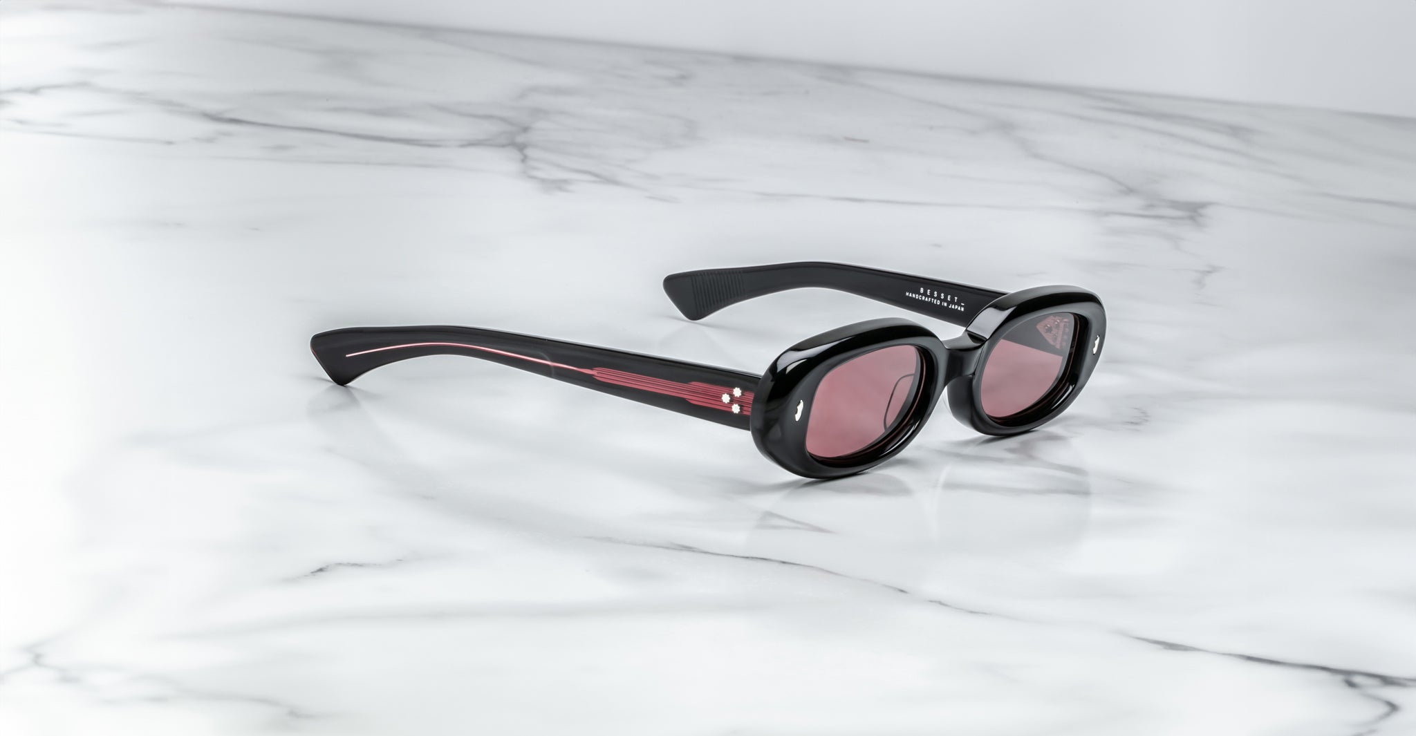 Jacques Marie Mage Besset black oval sunglasses with pink-tinted UV lenses, shown from above.