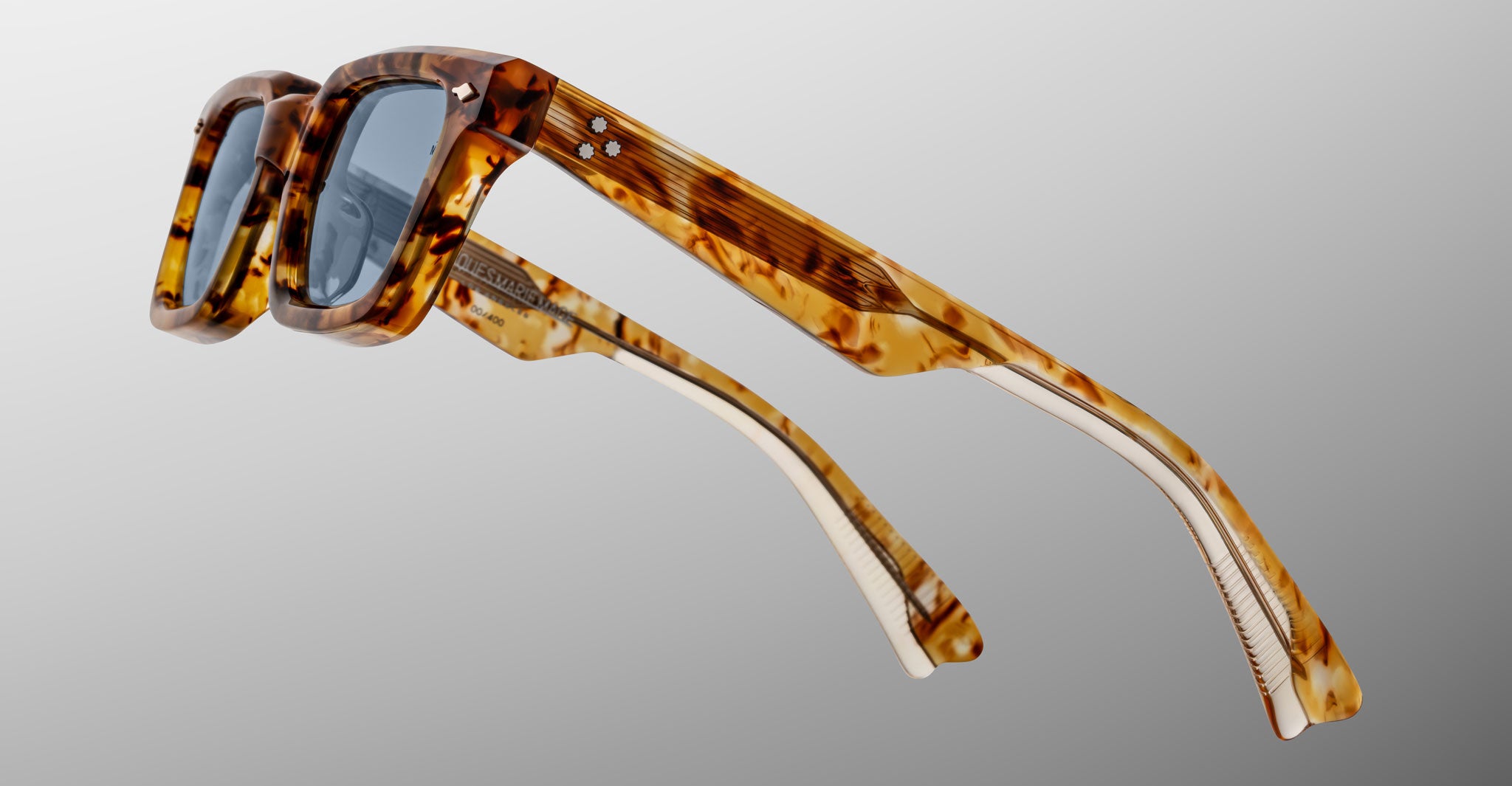 The Jacques Marie Mage Casablanca sunglasses, featuring thick tortoiseshell rectangular frames, blue-tinted lenses, and two silver rivets on the arms near the hinges, are displayed against a light gray background.