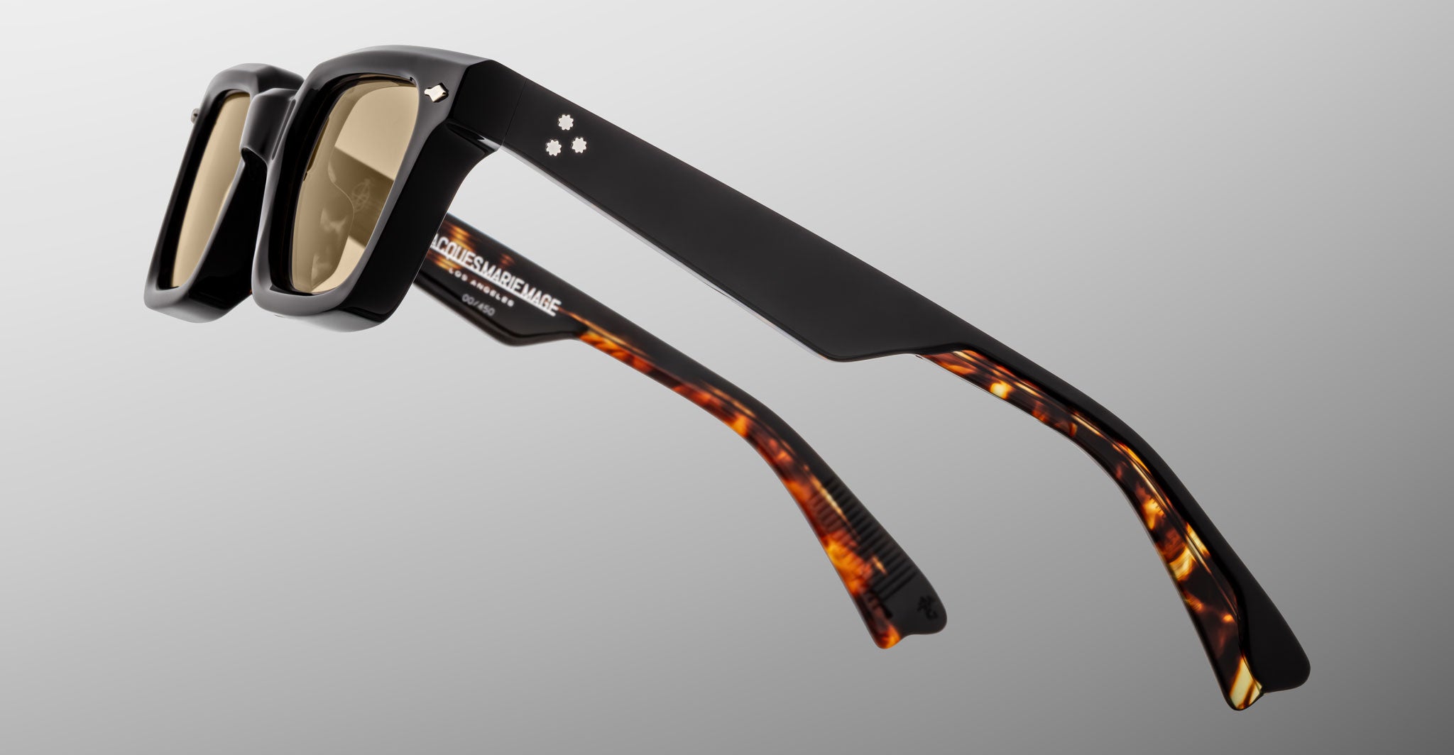 The Jacques Marie Mage Casablanca sunglasses feature thick black frames with brown-tinted lenses and brown tortoiseshell arms accented by black detailing near the hinges, set against a plain light gradient background.