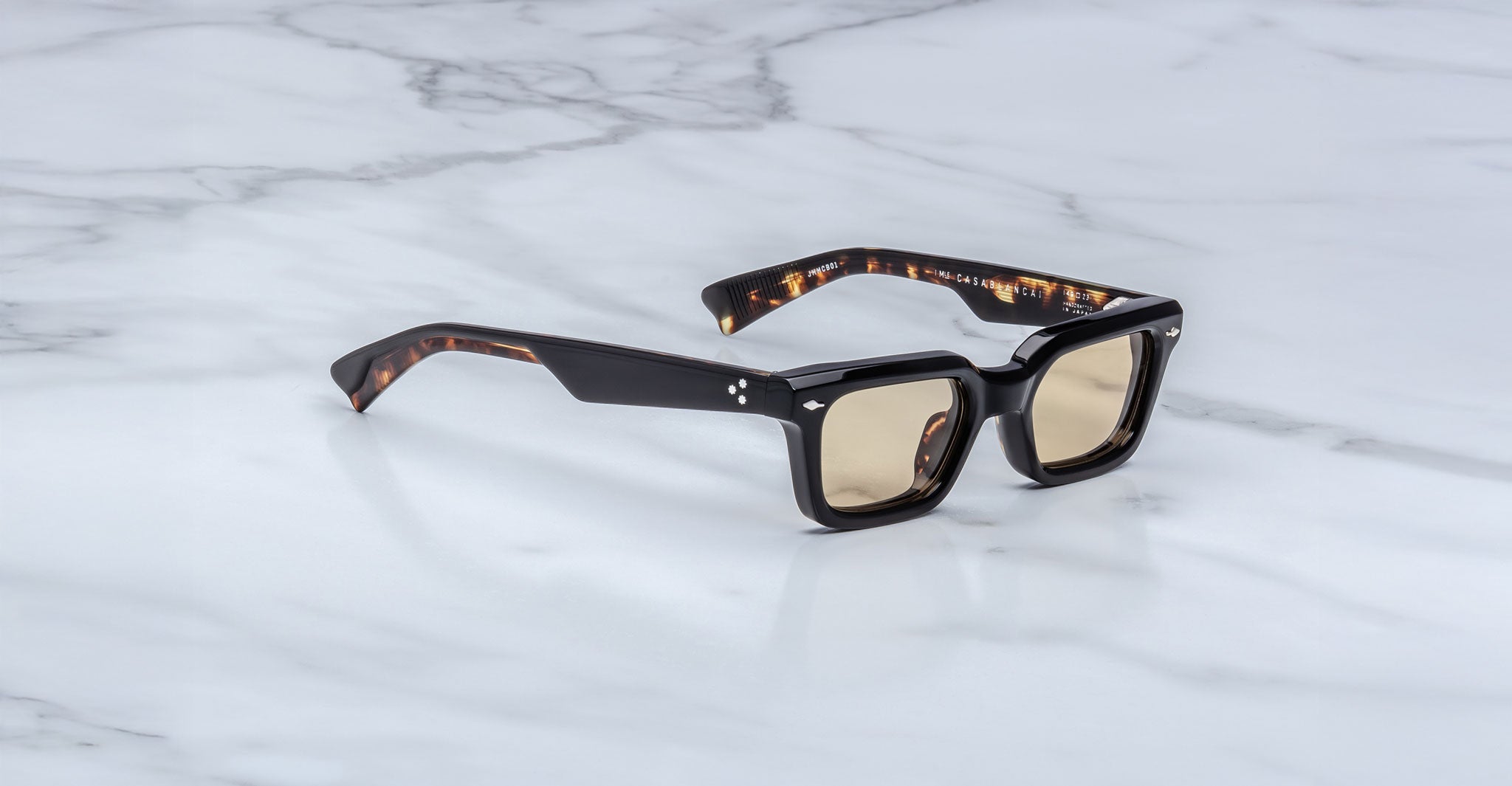 The Jacques Marie Mage Casablanca sunglasses, featuring thick dark tortoiseshell rectangular frames and light brown lenses, rest on a white marble surface.