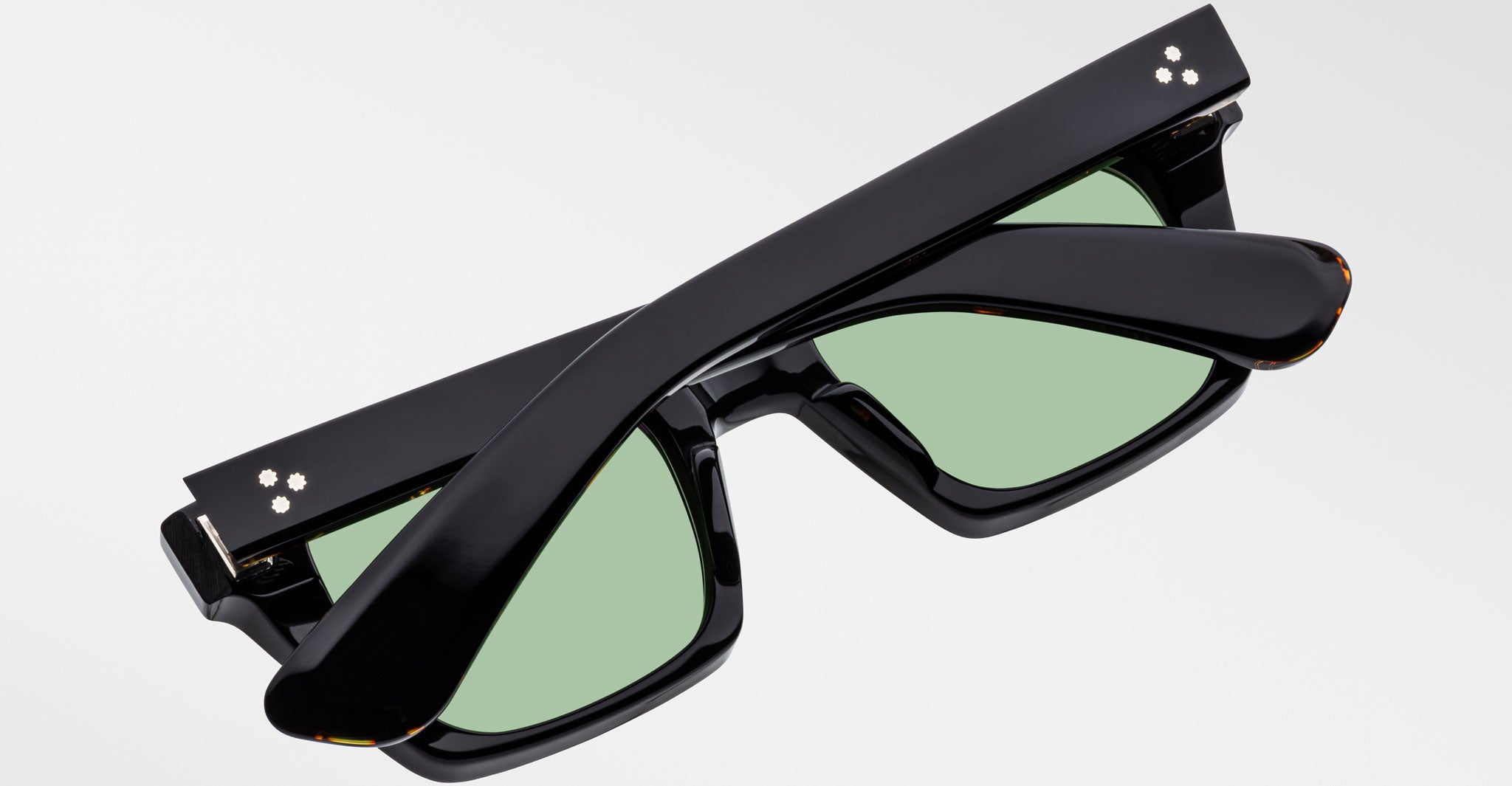 Jacques Marie Mage Quentin black sunglasses with green lenses, folded, top-down view; designer eyewear.