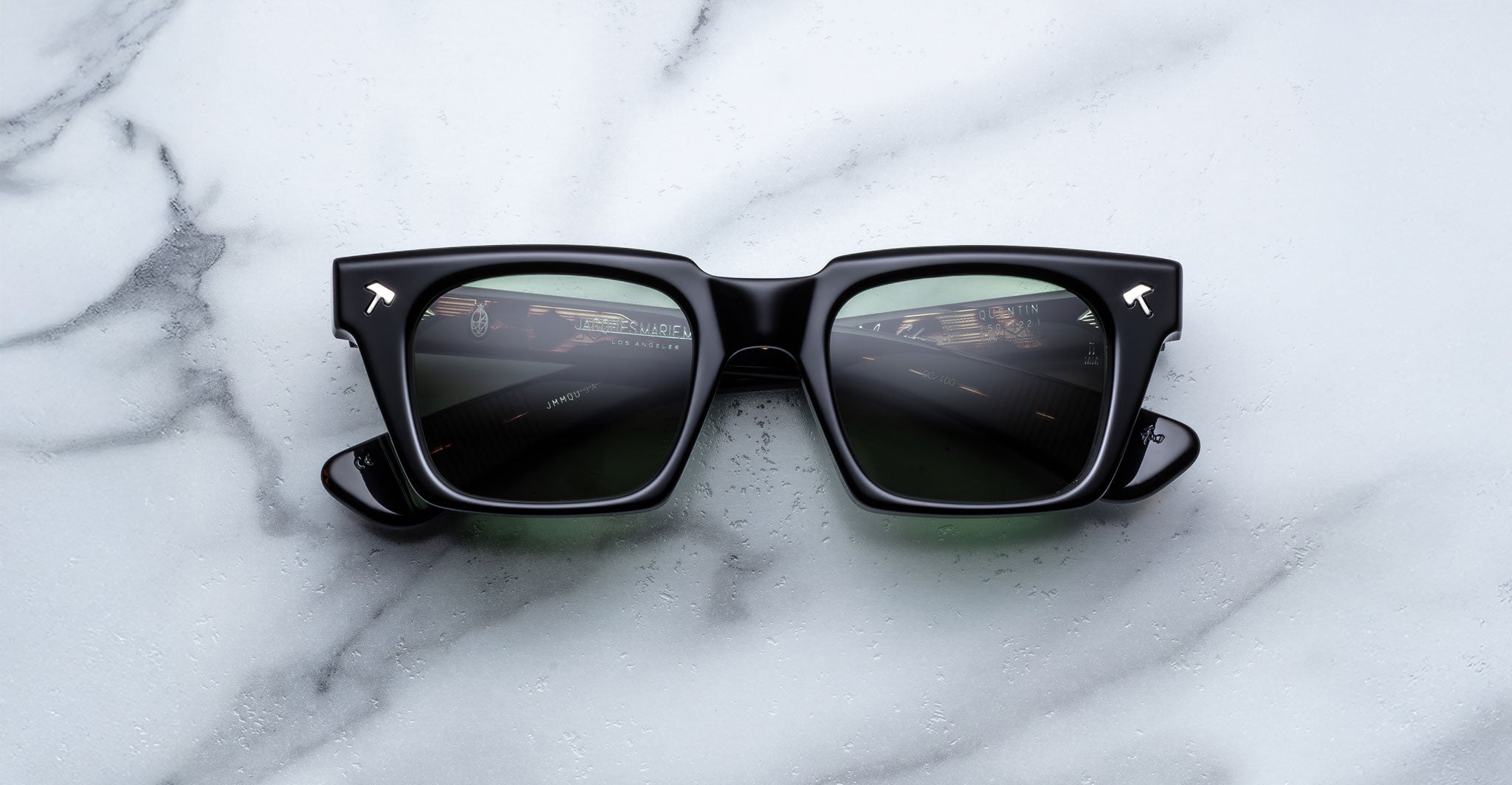 Jacques Marie Mage Quentin sunglasses with thick frames shown from above, road reflection visible in lenses.
