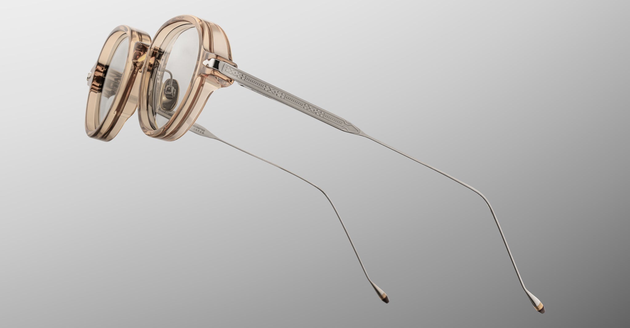 The Jacques Marie Mage Clark frames by Jacques Marie Mage feature transparent round rims and slim metal temples, styled in a midcentury-inspired design and displayed from a side angle on a neutral background.