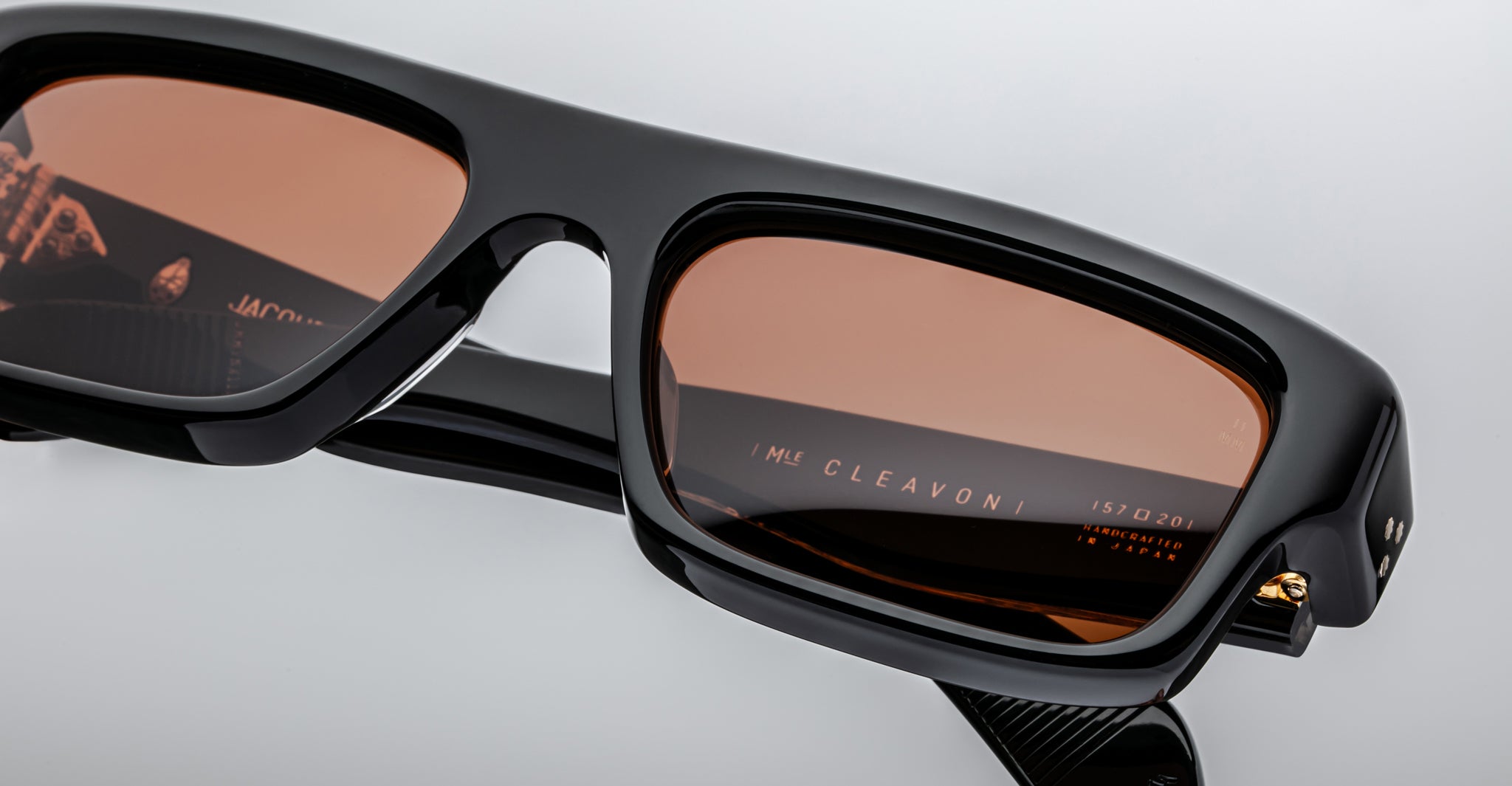 Close-up of Jacques Marie Mage Cleavon 57 sunglasses, black rectangular frame, brown lenses, gold accents, UV protection.