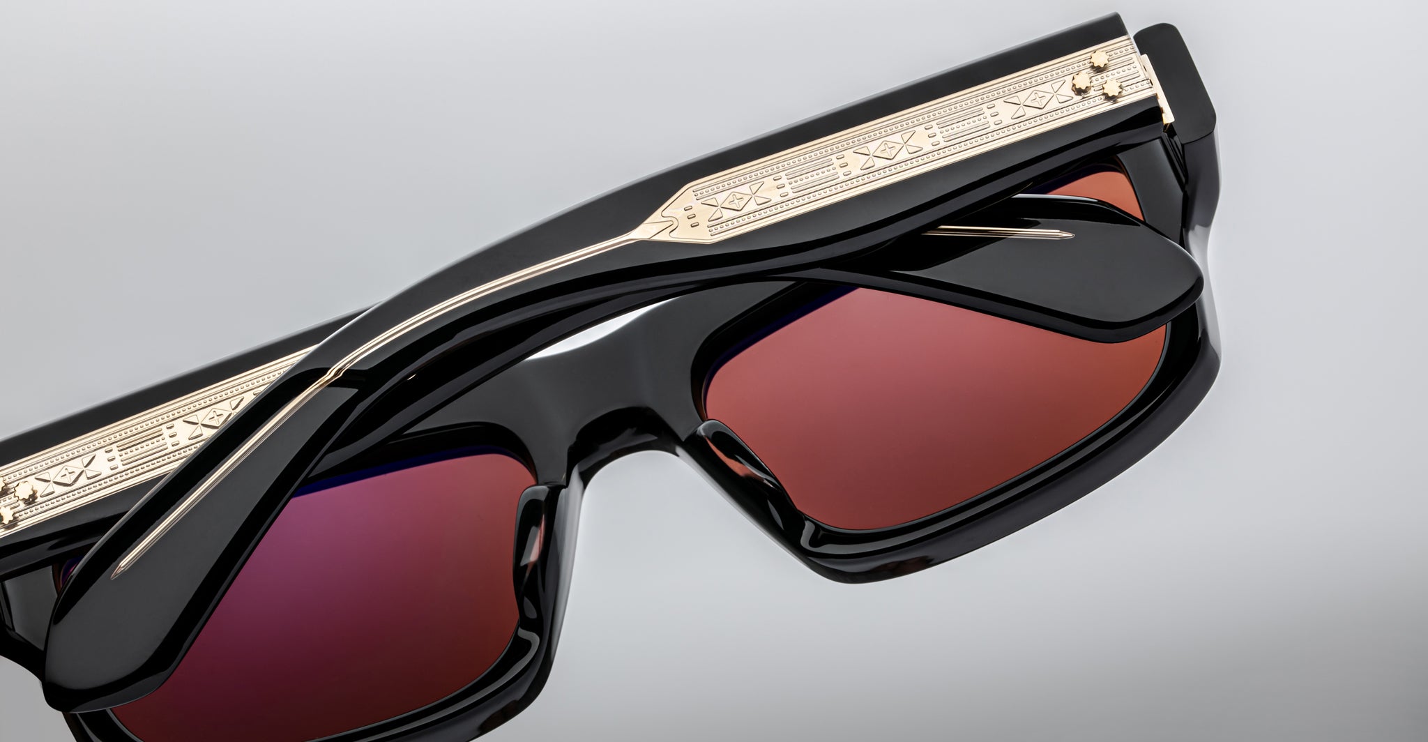 Close-up of Jacques Marie Mage Cleavon 57 sunglasses, black frame with gold accents and red-tinted lenses, front angle view.