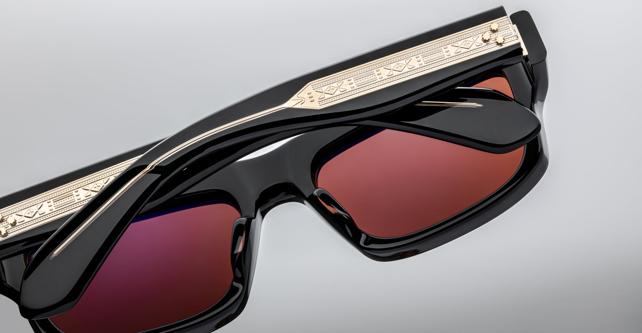 Close-up of Jacques Marie Mage Cleavon 57 sunglasses, black frame with gold accents and red-tinted lenses, front angle view.