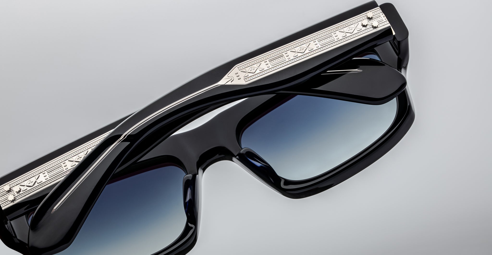 Close-up of Jacques Marie Mage Cleavon 57 sunglasses, featuring black frames, blue gradient lenses, and silver engraved arms.