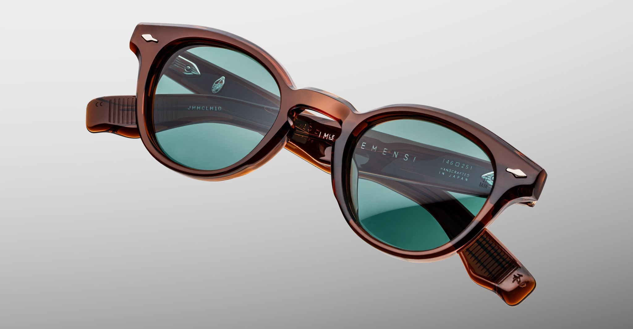 Jacques Marie Mage Clemens sunglasses feature brown acetate frames and round green-tinted lenses, shown on a light gray background—a luxurious, limited-edition design for those who value timeless style.