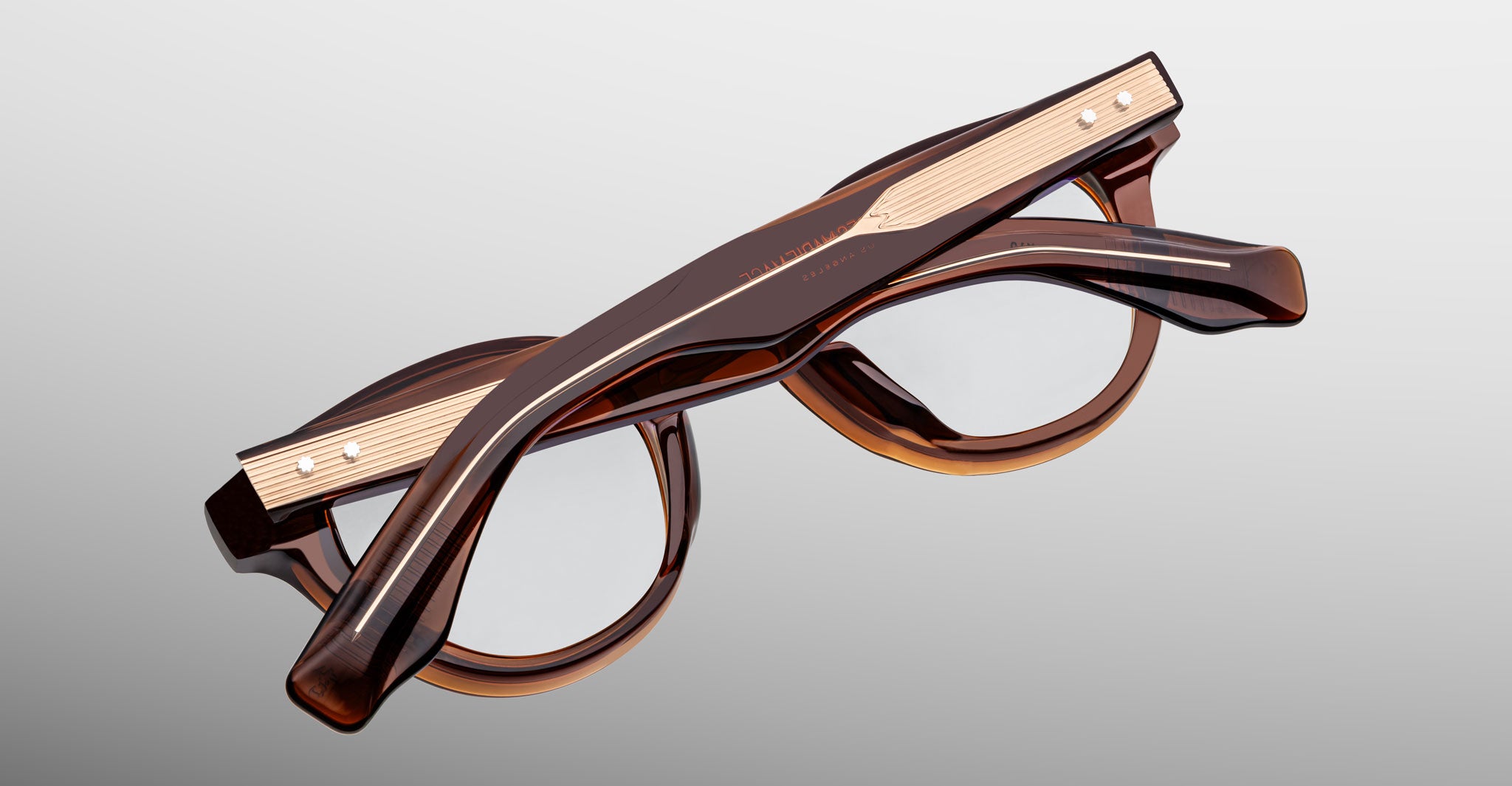 Jacques Marie Mage Clemens in Hickory brown eyeglasses with gold-accented arms, shown upside down; top view highlights frame and arm details.