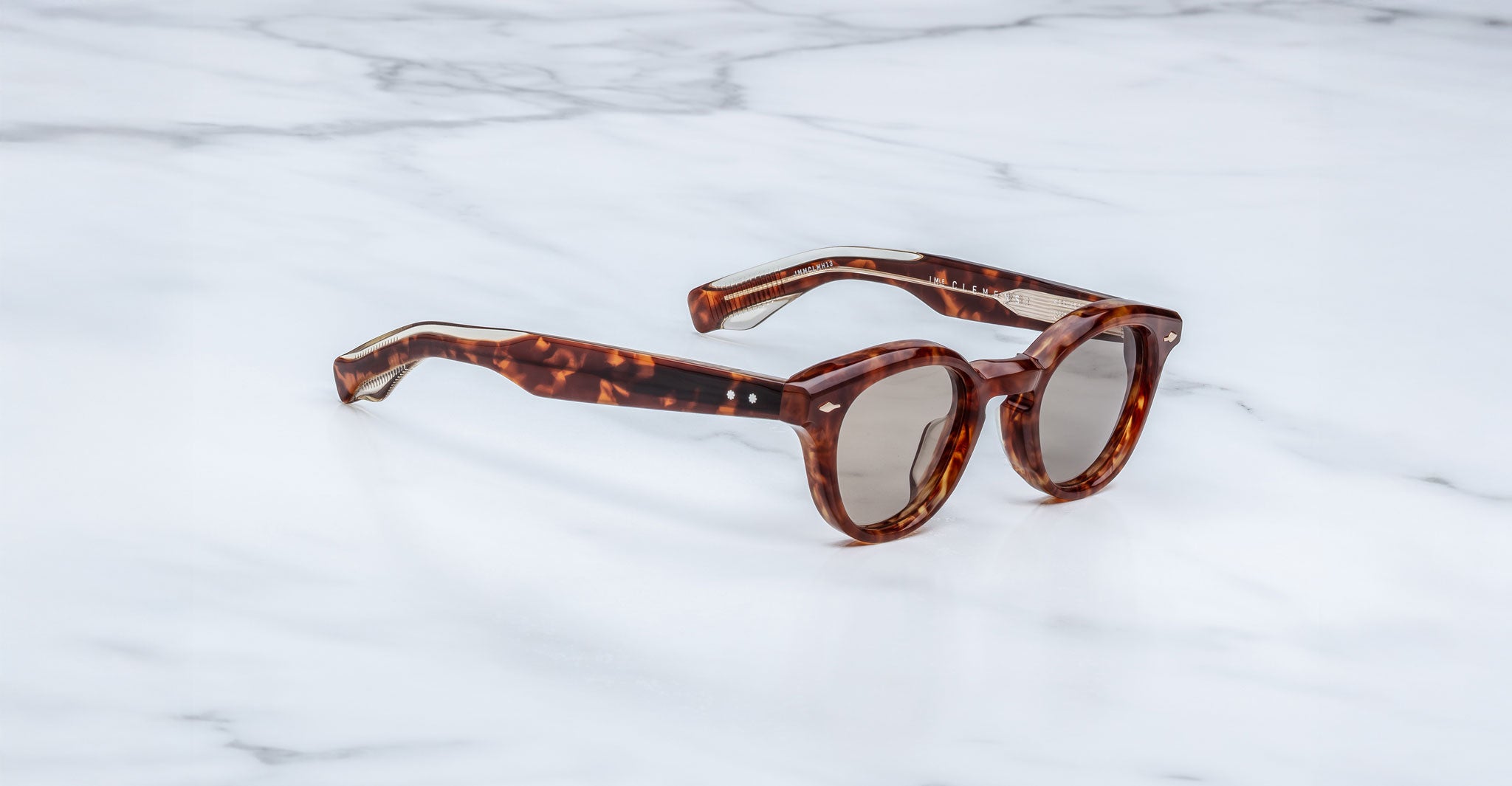 Jacques Marie Mage Clemens tortoiseshell sunglasses with round lenses and thick frames rest on white marble—sophisticated, limited-edition eyewear for the discerning collector.