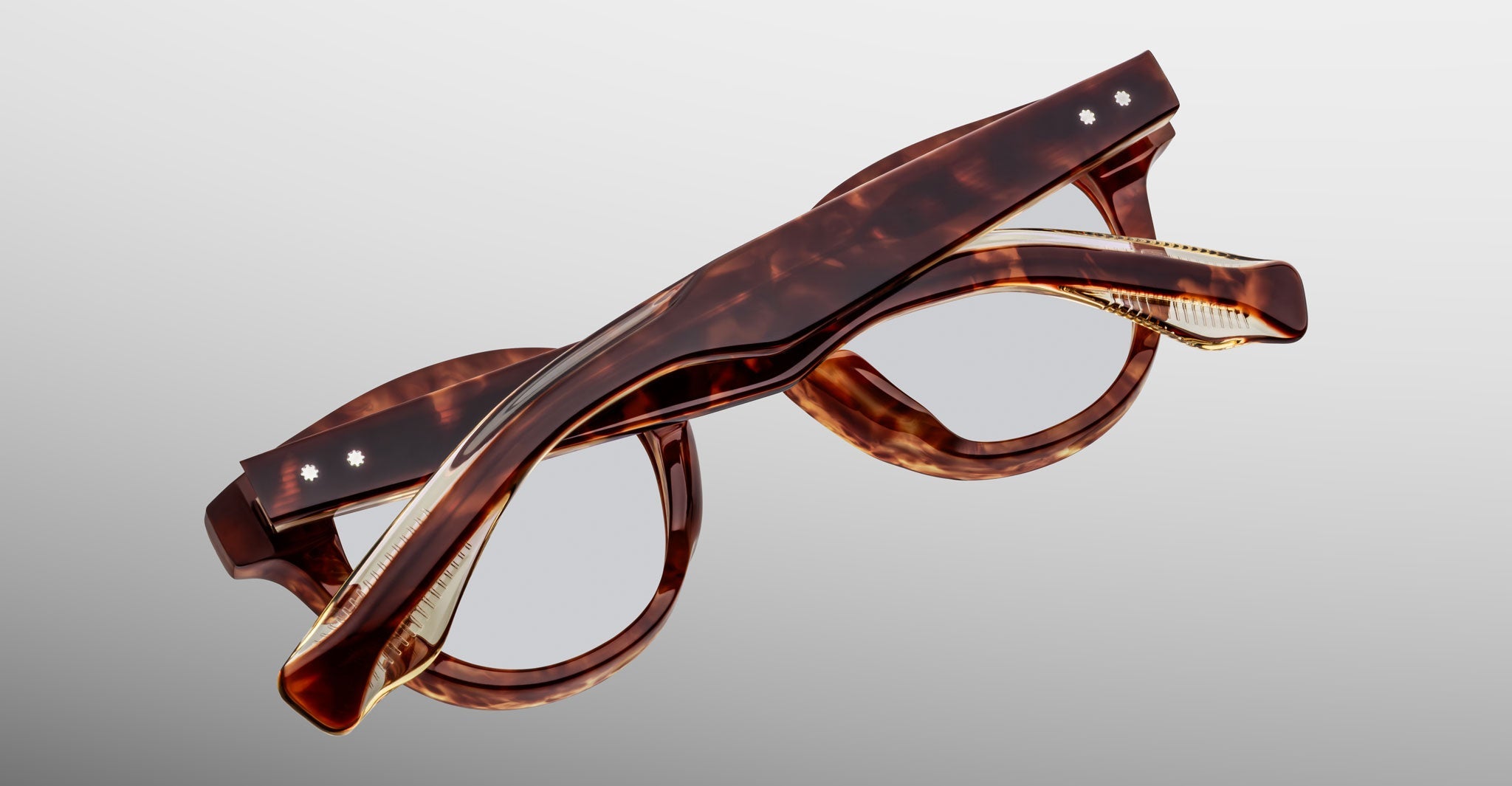 The Jacques Marie Mage Clemens limited-edition spectacles by Jacques Marie Mage feature a tortoiseshell pattern and folding hinges, shown partially folded on a light gray background.