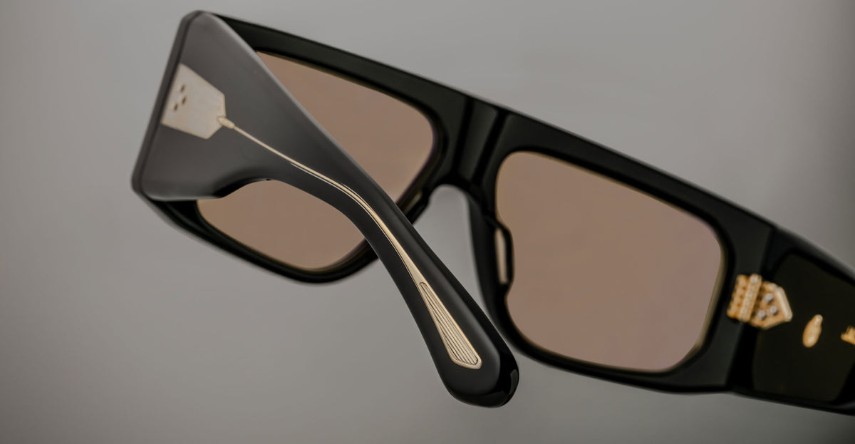 Close-up of Jacques Marie Mage Cliff rectangular black sunglasses with gold temples and hinges, viewed from the side.