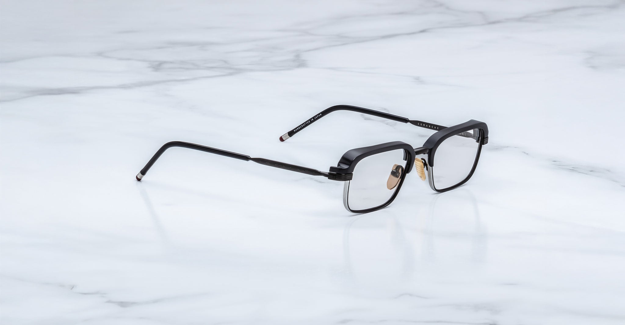 A pair of Jacques Marie Mage Comanche black rectangular eyeglasses with metal temples rests on a white marble surface, showcasing the brand’s limited-edition craftsmanship.