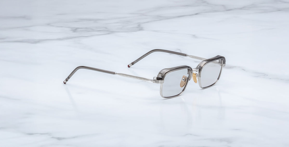 A pair of rectangular, translucent Jacques Marie Mage Comanche eyeglasses with thin arms rests on a white marble surface—a limited-edition design from Jacques Marie Mage.