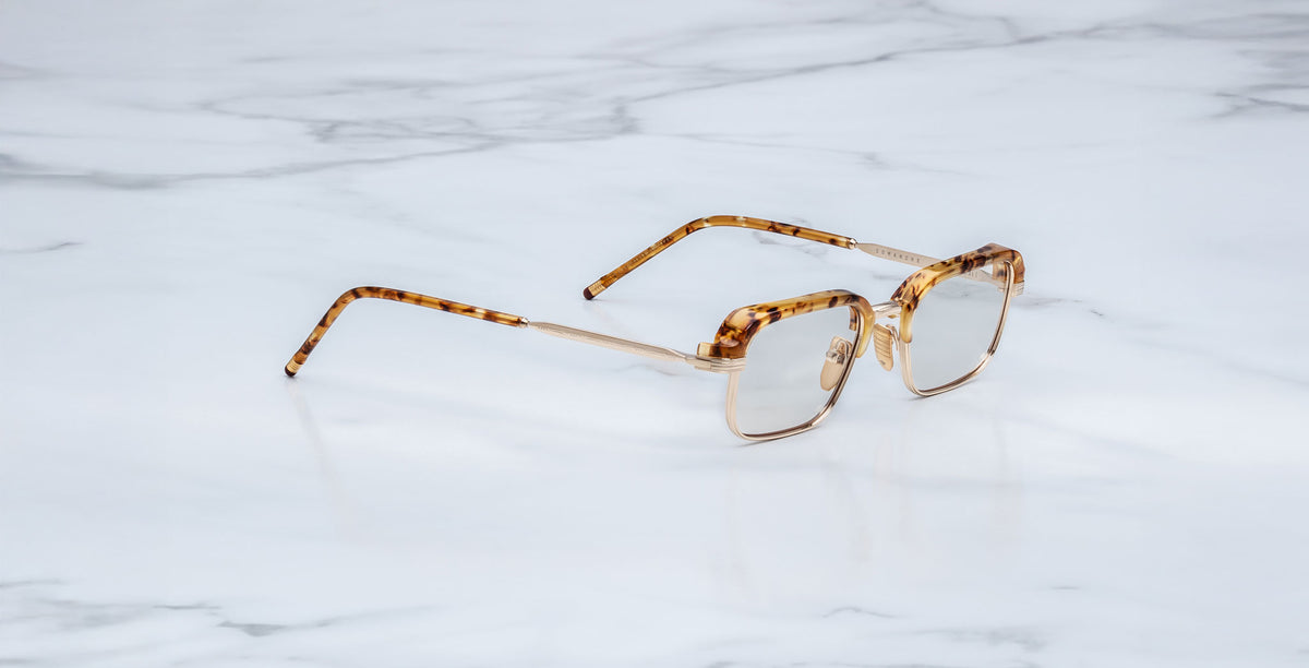 The Jacques Marie Mage Comanche rectangular tortoiseshell eyeglasses, known for their thin frames and limited-edition design, rest on a white marble surface.