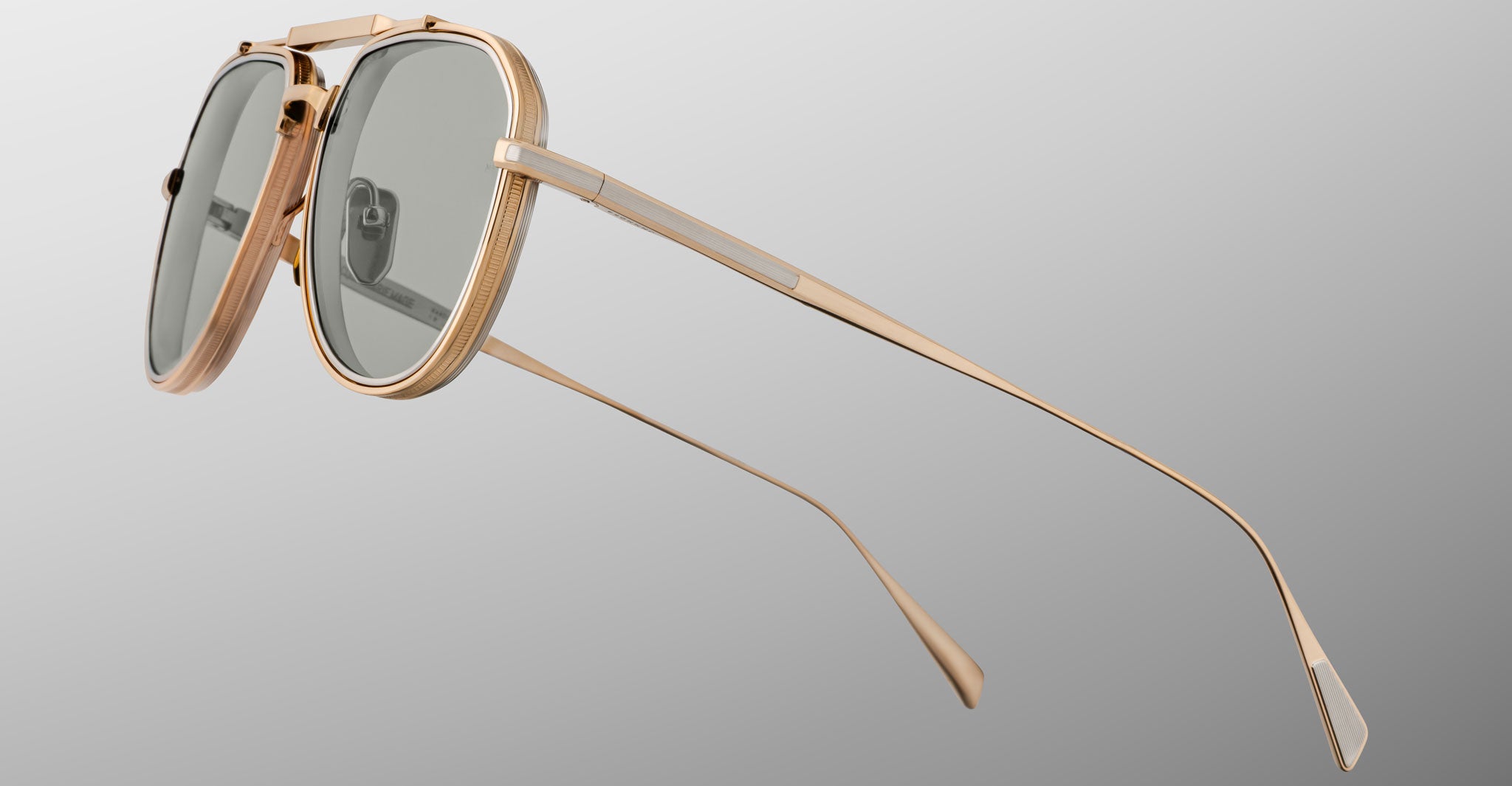 The Jacques Marie Mage Commander sunglasses feature gold frames, gray-tinted oval lenses, and slim temples, displayed at an angle on a plain gray background.