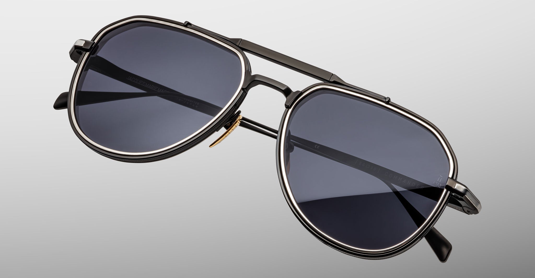 Close-up of Jacques Marie Mage Commander aviator-style sunglasses in black with dark lenses and a double bridge, set against a plain light gray background.