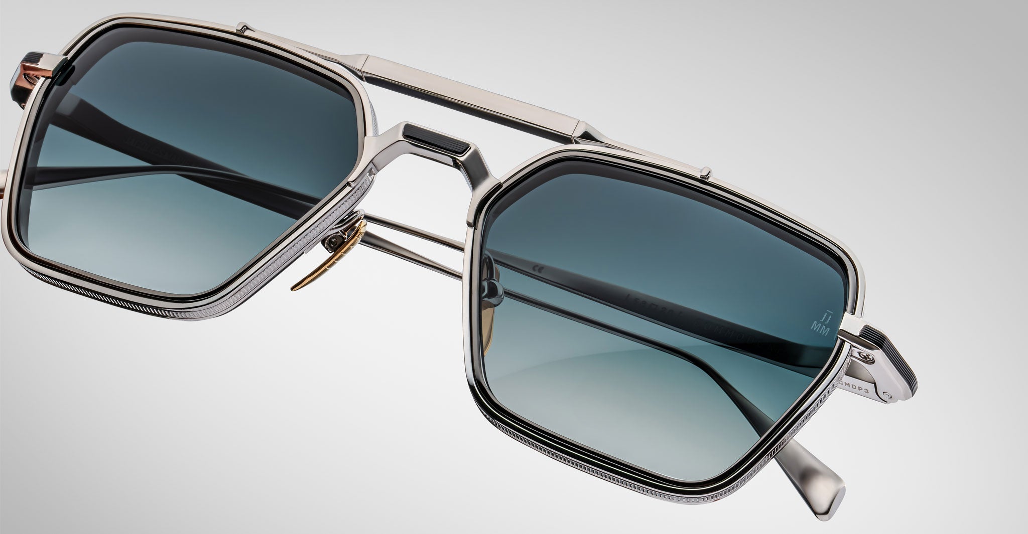 Close-up of Jacques Marie Mage Commodore sunglasses featuring square blue-tinted lenses, silver metal frames, a double bridge, and thin temples, set against a light gray gradient background.