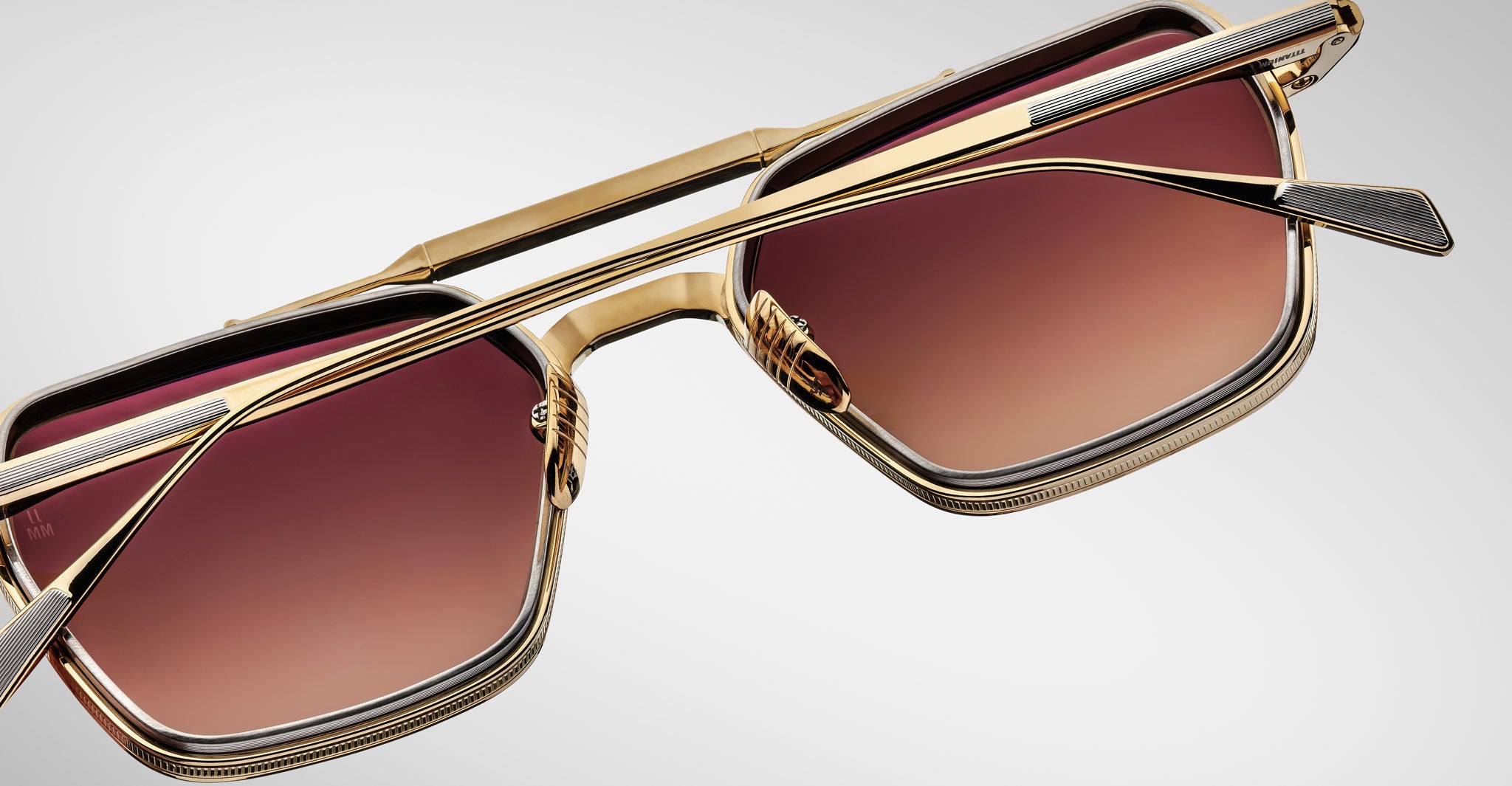 Close-up of Jacques Marie Mage Commodore sunglasses featuring gold square frames, brown gradient lenses, unique double bridges, and detailed accents on the arms and edges, shown against a plain white background.