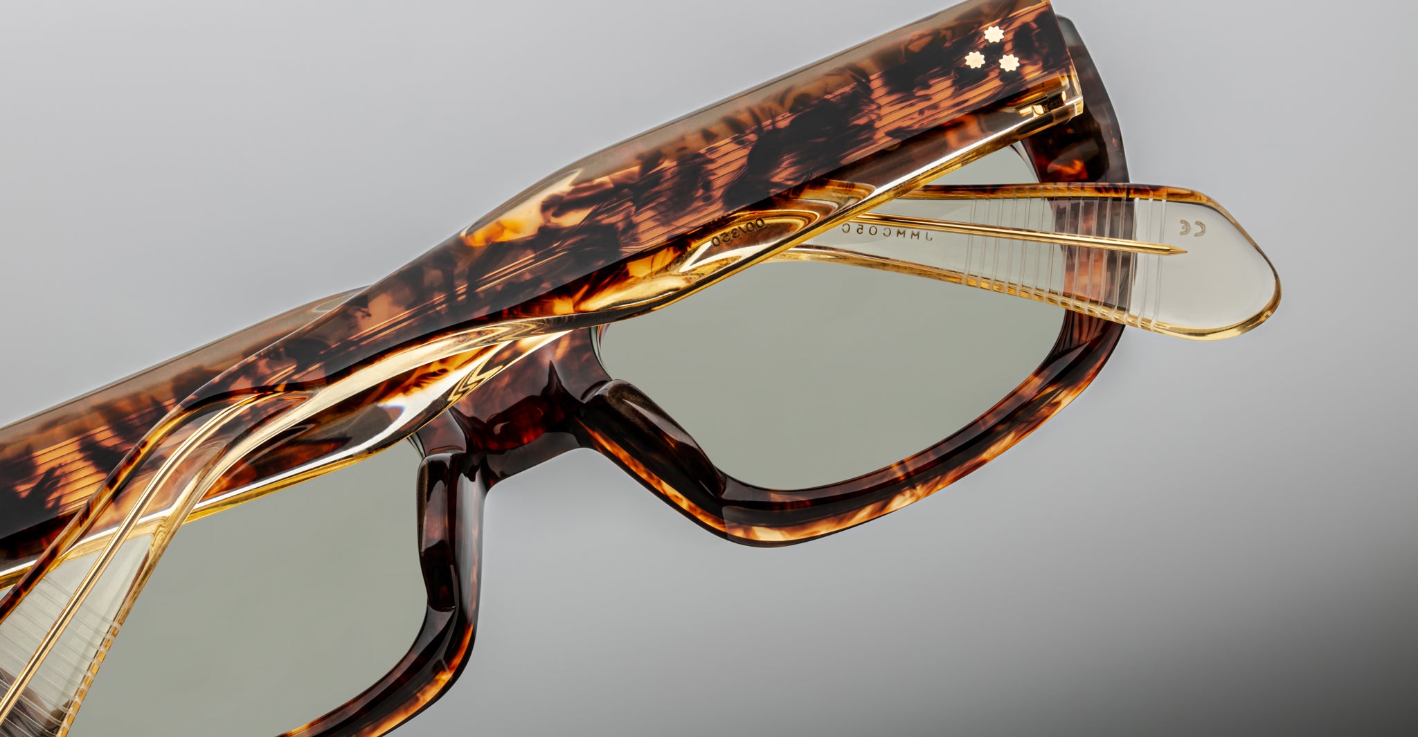 Close-up of Jacques Marie Mage Corniche sunglasses with thick rectangular tortoiseshell frames, green-tinted lenses, and transparent arms showcased in detail.