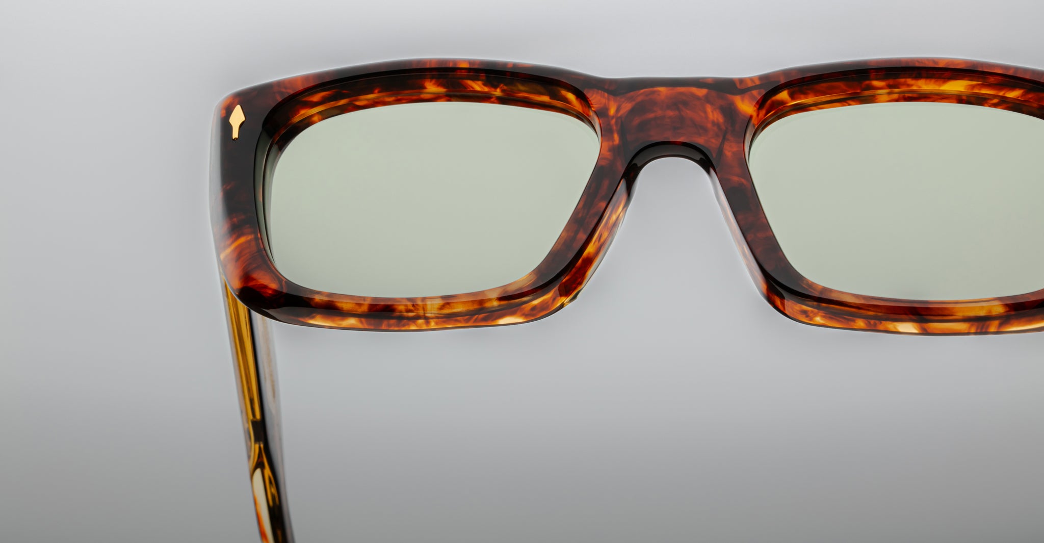 Close-up of the upper half of Jacques Marie Mage Corniche tortoiseshell square eyeglass frames with slightly tinted lenses, set against a plain gray background.