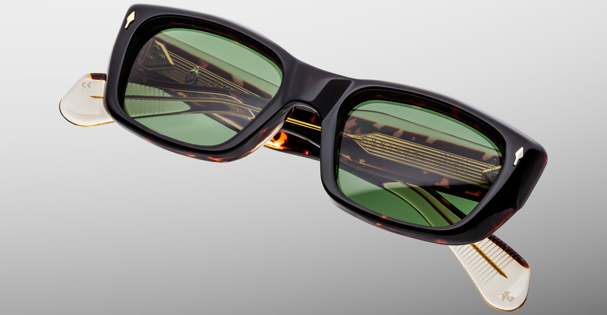The Jacques Marie Mage Corniche sunglasses feature rectangular dark tortoiseshell frames, green tinted lenses, and gold temple detailing, showcased against a light gray background.