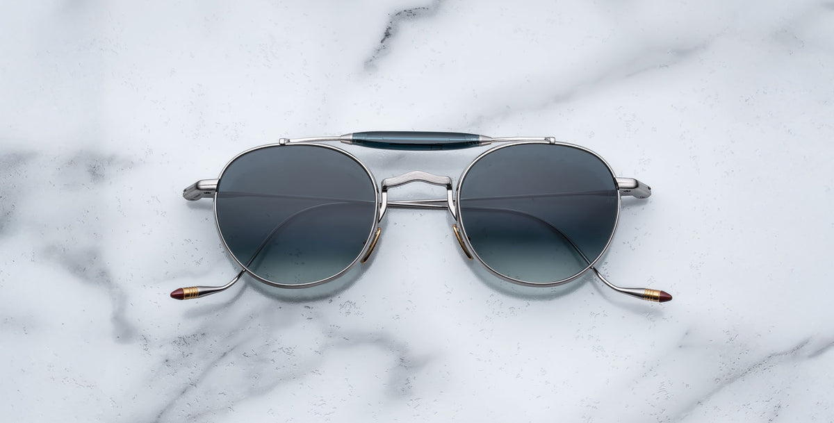 Front view of the Jacques Marie Mage Dasan titanium sunglass in silver with blue gradient lenses on a white marbled with grey veining background