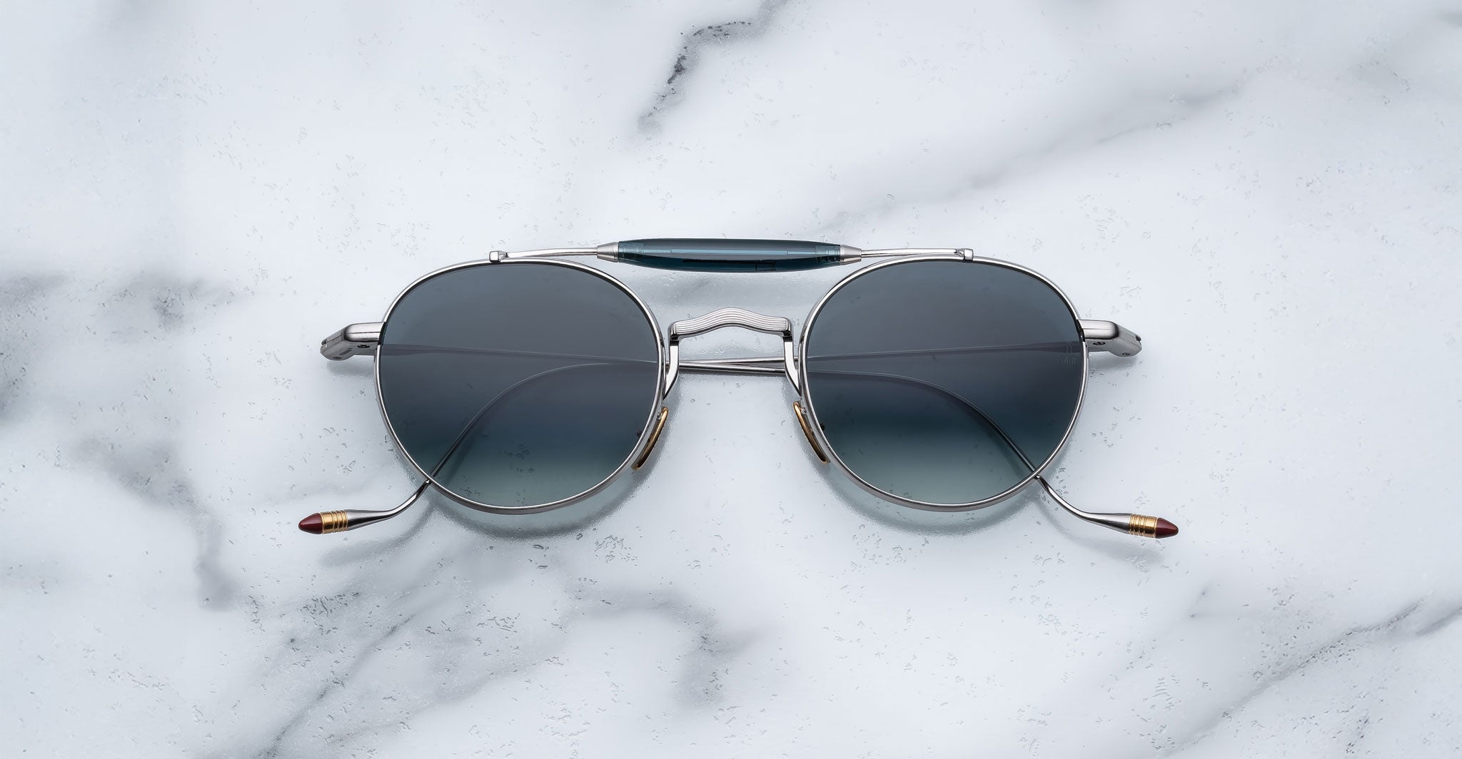 Front view of the Jacques Marie Mage Dasan titanium sunglass in silver with blue gradient lenses on a white marbled with grey veining background