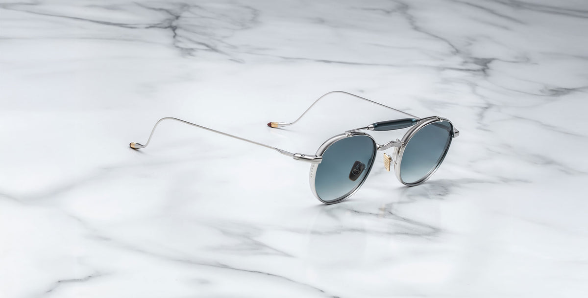 Profile view of the Jacques Marie Mage Dasan titanium sunglass in silver with blue gradient lenses on a white marbled with grey veining background