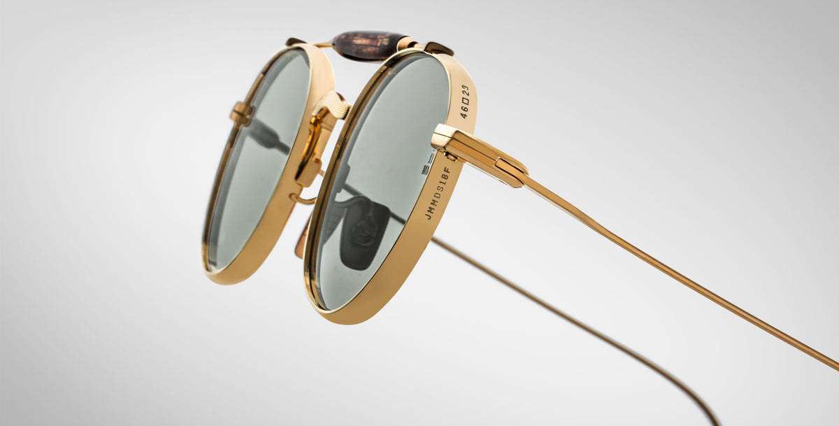 Detailed profile view of the Jacques Marie Mage Dasan titanium sunglass in gold color with light grey lenses on a white background