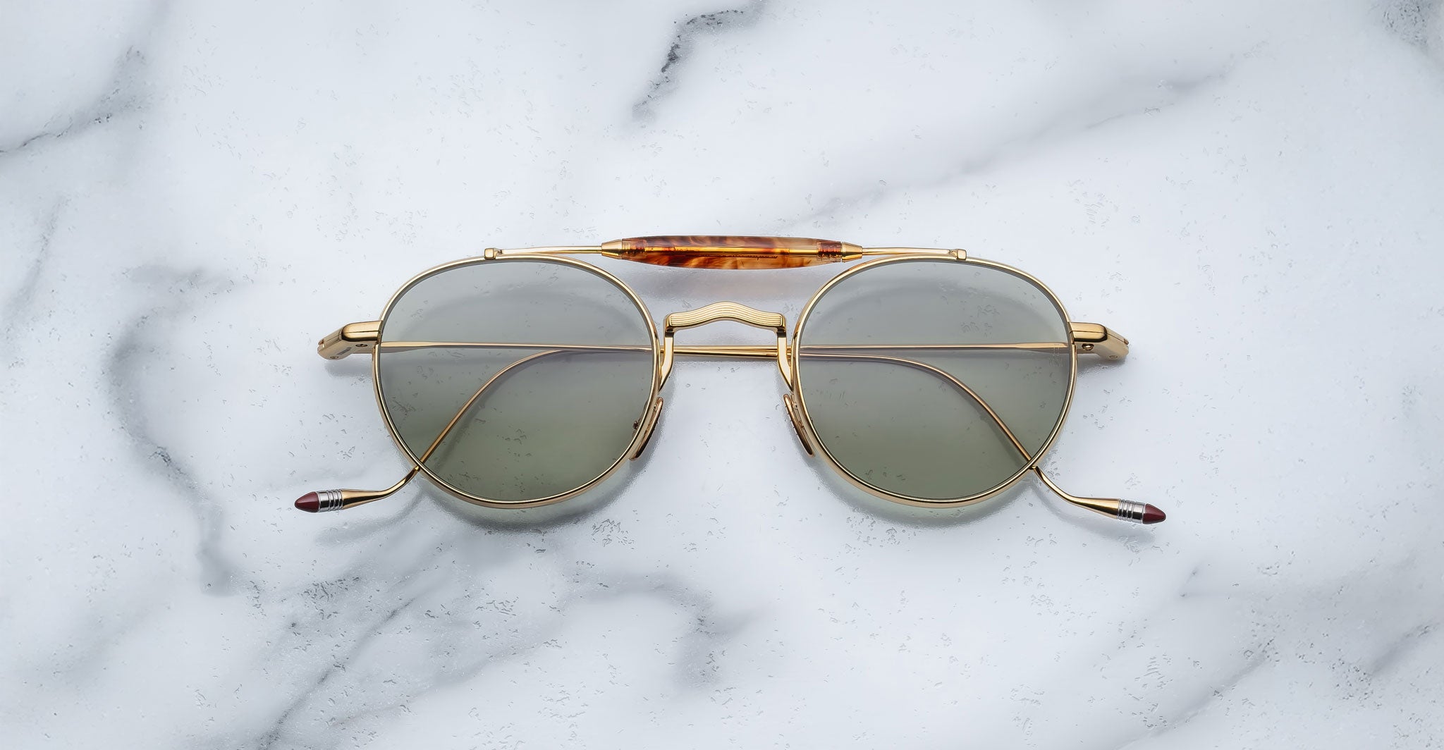Front view of the Jacques Marie Mage Dasan titanium sunglass in gold color with light grey lenses on a white marbled with grey veining background