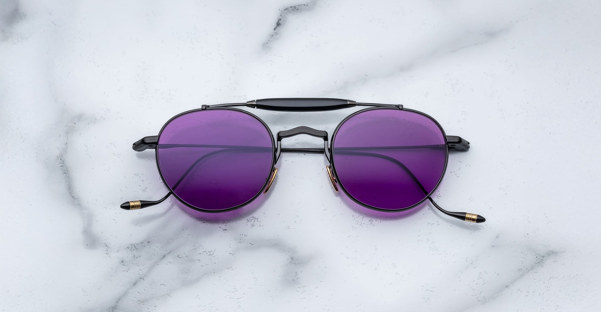 Front view of the Jacques Marie Mage Dasan titanium sunglass in black color with purple lenses on a white marbled with grey veining background