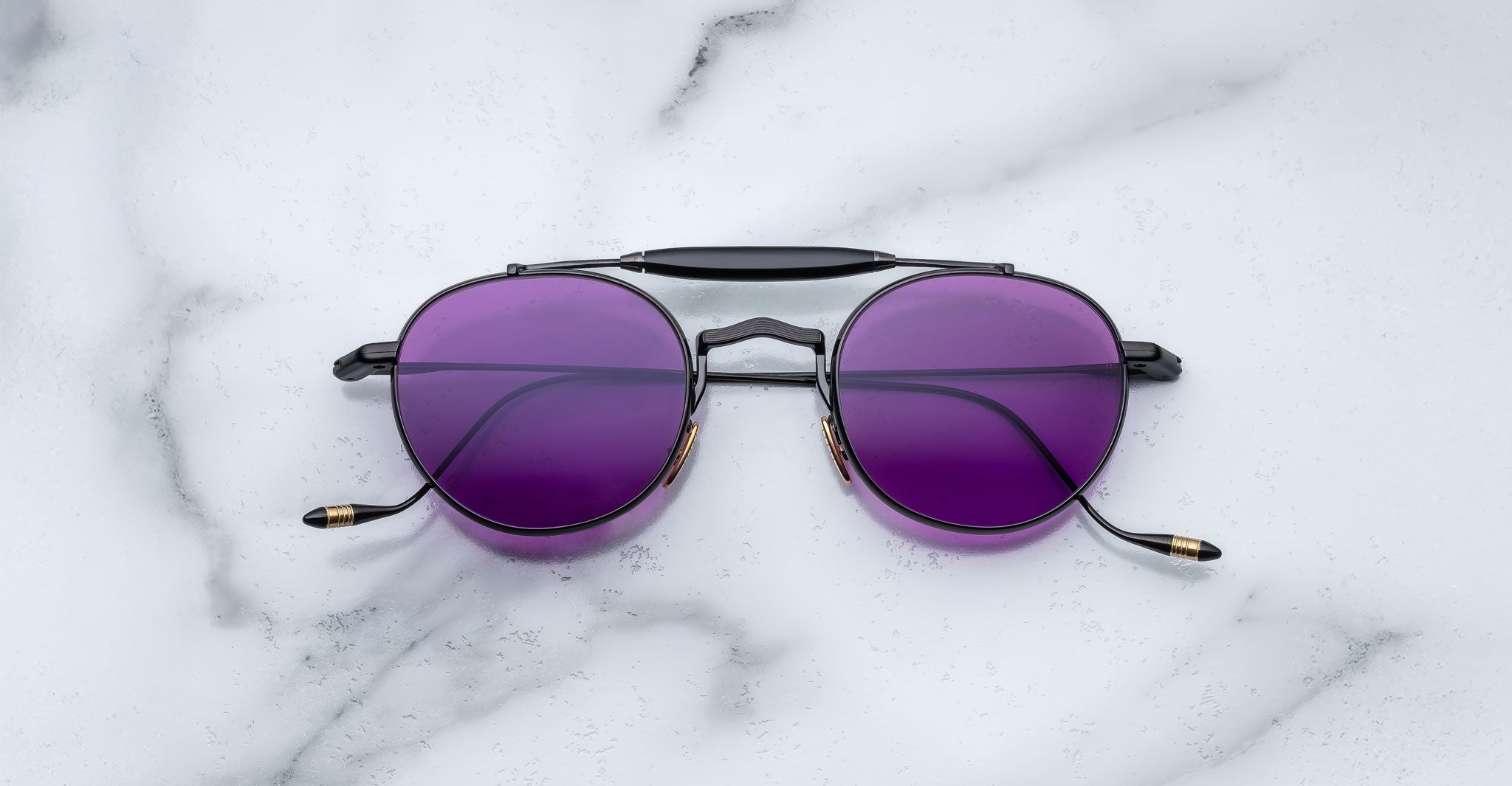 Front view of the Jacques Marie Mage Dasan titanium sunglass in black color with purple lenses on a white marbled with grey veining background
