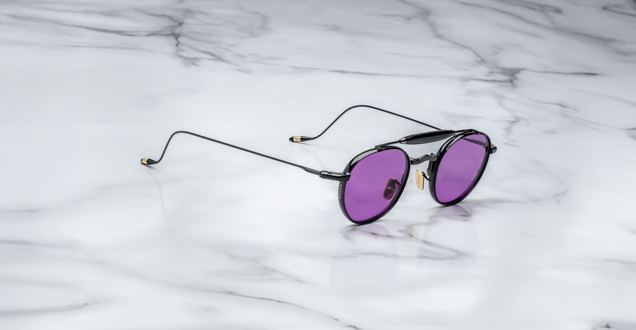 Profile view of the Jacques Marie Mage Dasan titanium sunglass in black color with purple lenses on a white marbled with grey veining background