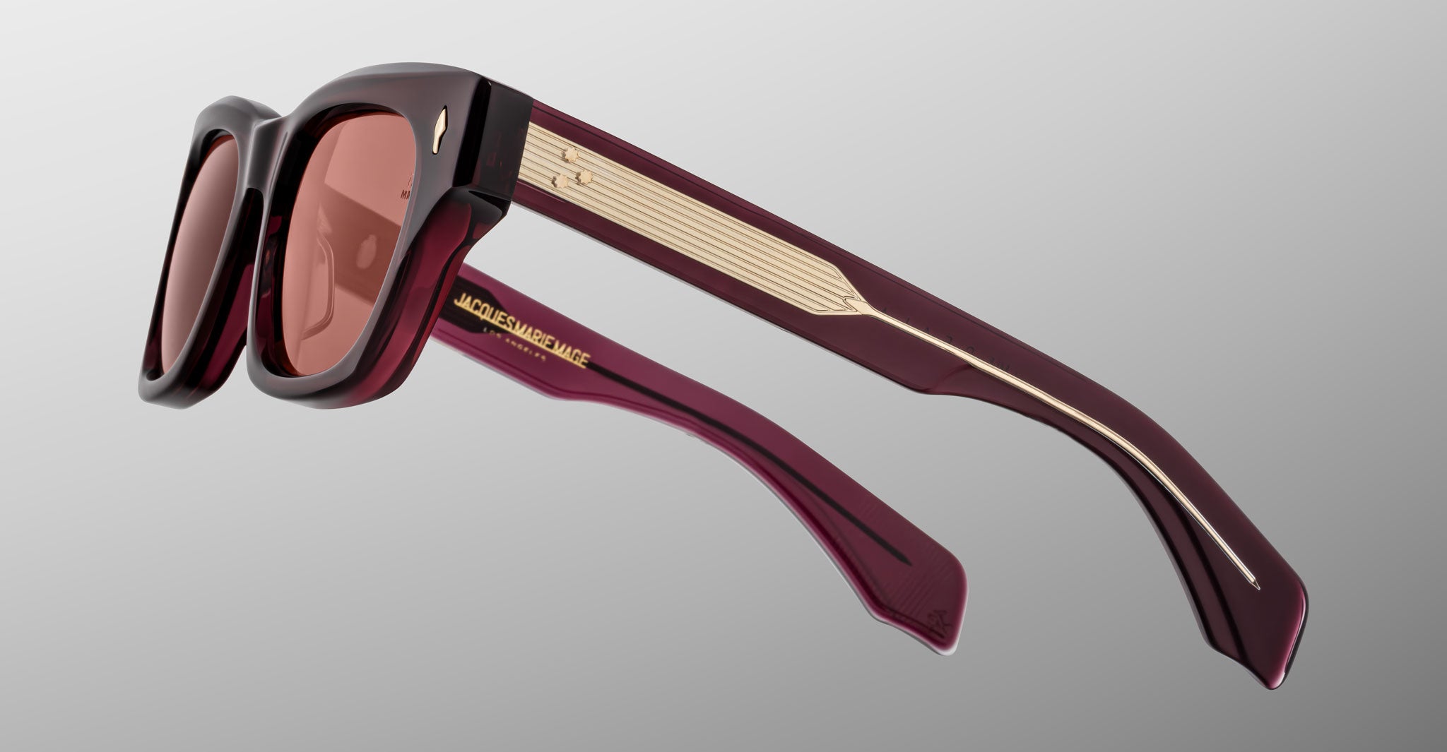 The Jacques Marie Mage Dealan 53 features rectangular sunglasses with thick burgundy frames, matching tinted lenses, gold-detailed arms, and the brand name in gold on the inner side.