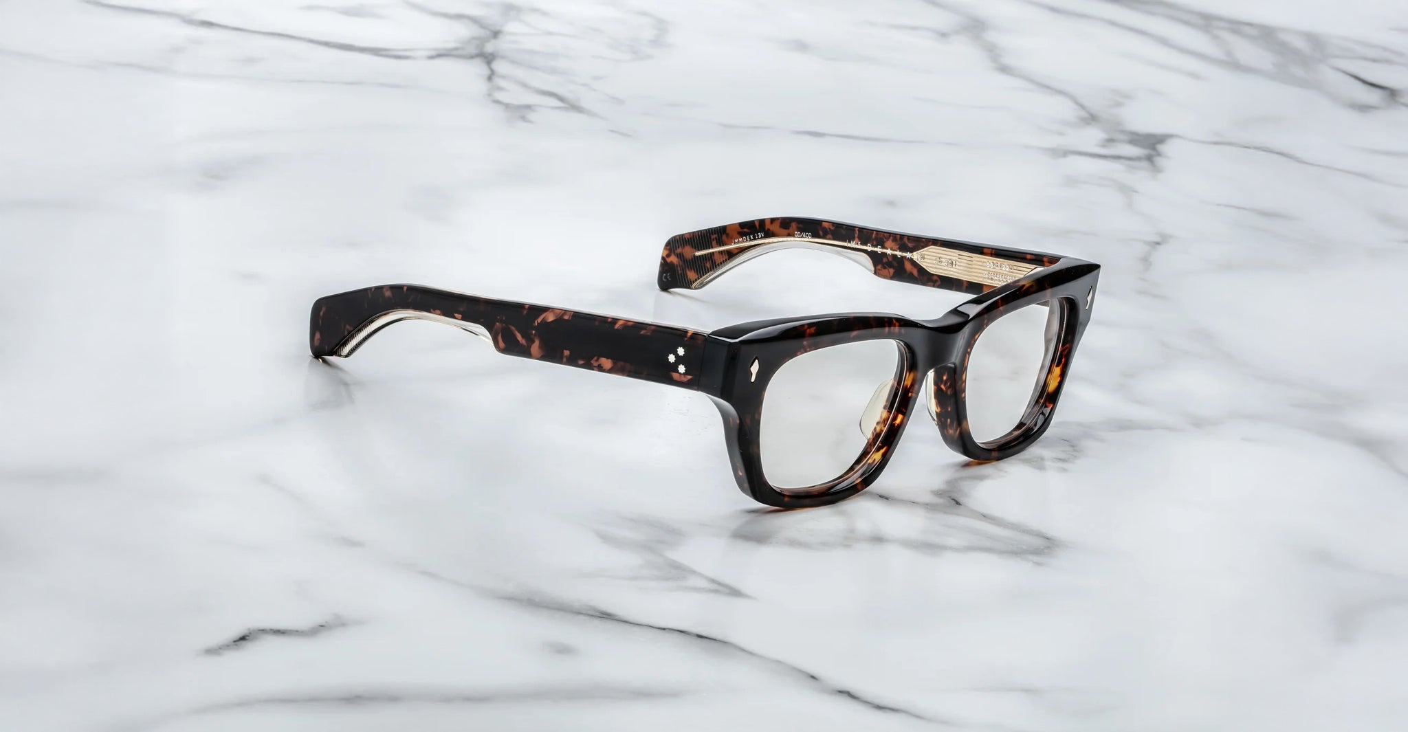 A Jacques Marie Mage Dealan 53 rectangular eyeglasses with a tortoiseshell frame rest on a white marble surface.
