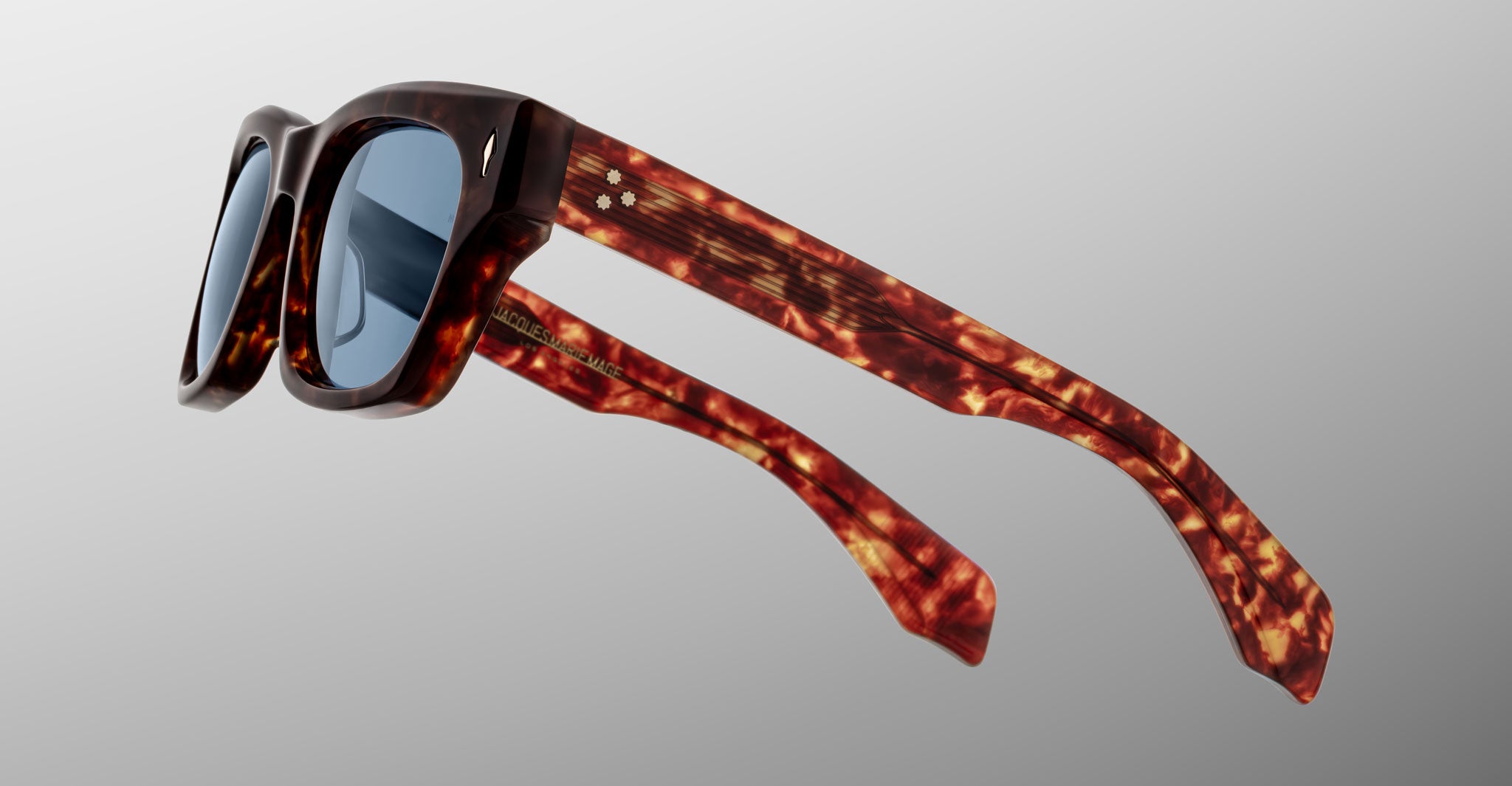 The Jacques Marie Mage Dealan 53 sunglasses feature tortoiseshell-patterned plastic frames and blue-tinted lenses, shown against a plain light gray background.