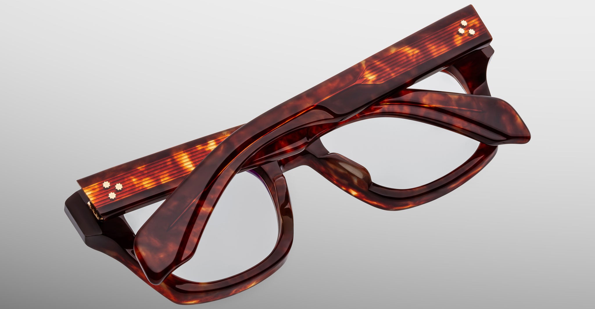 A close-up of Jacques Marie Mage Dealan 53 dark tortoiseshell rectangular eyeglasses, folded and stacked on a plain light gray background.