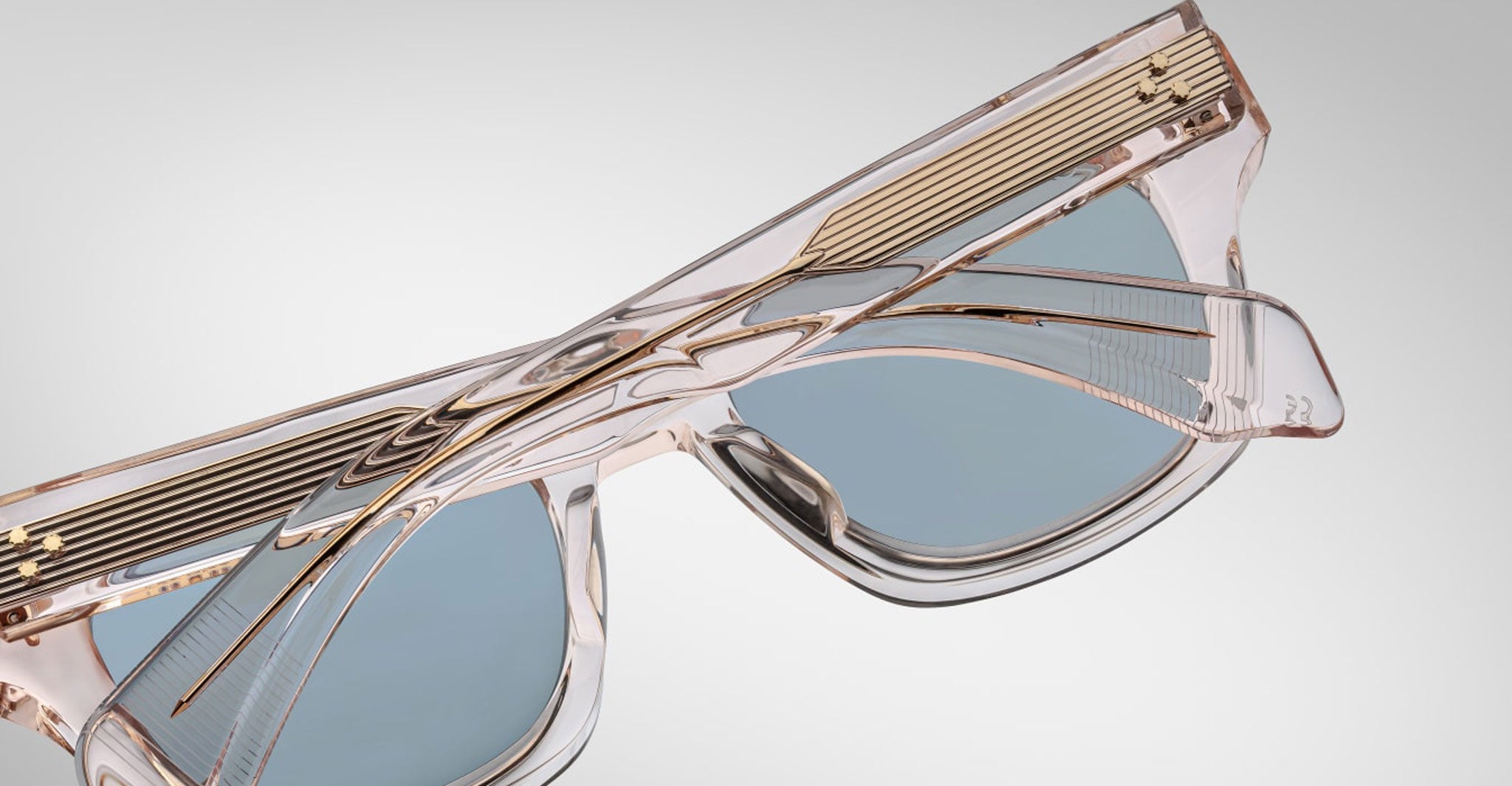 Close-up view of the Jacques Marie Mage Dealan 53 sunglasses, featuring translucent rectangular frames, light blue lenses, and gold-accented arms against a plain, light background.
