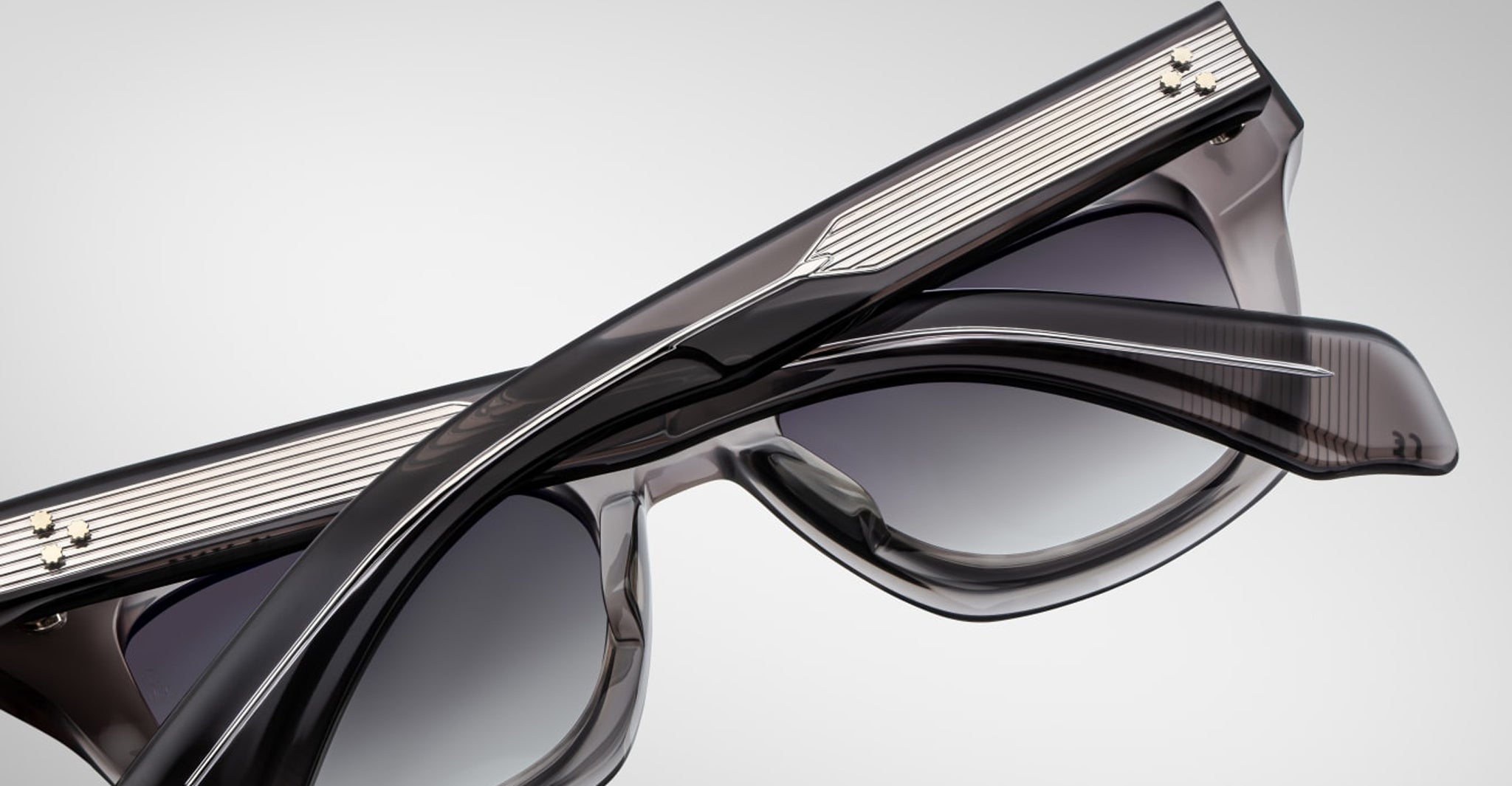 A close-up of two Jacques Marie Mage Dealan 53 black sunglasses with gradient lenses, stacked together, featuring detailed frames with thin silver stripes and metallic corner accents.