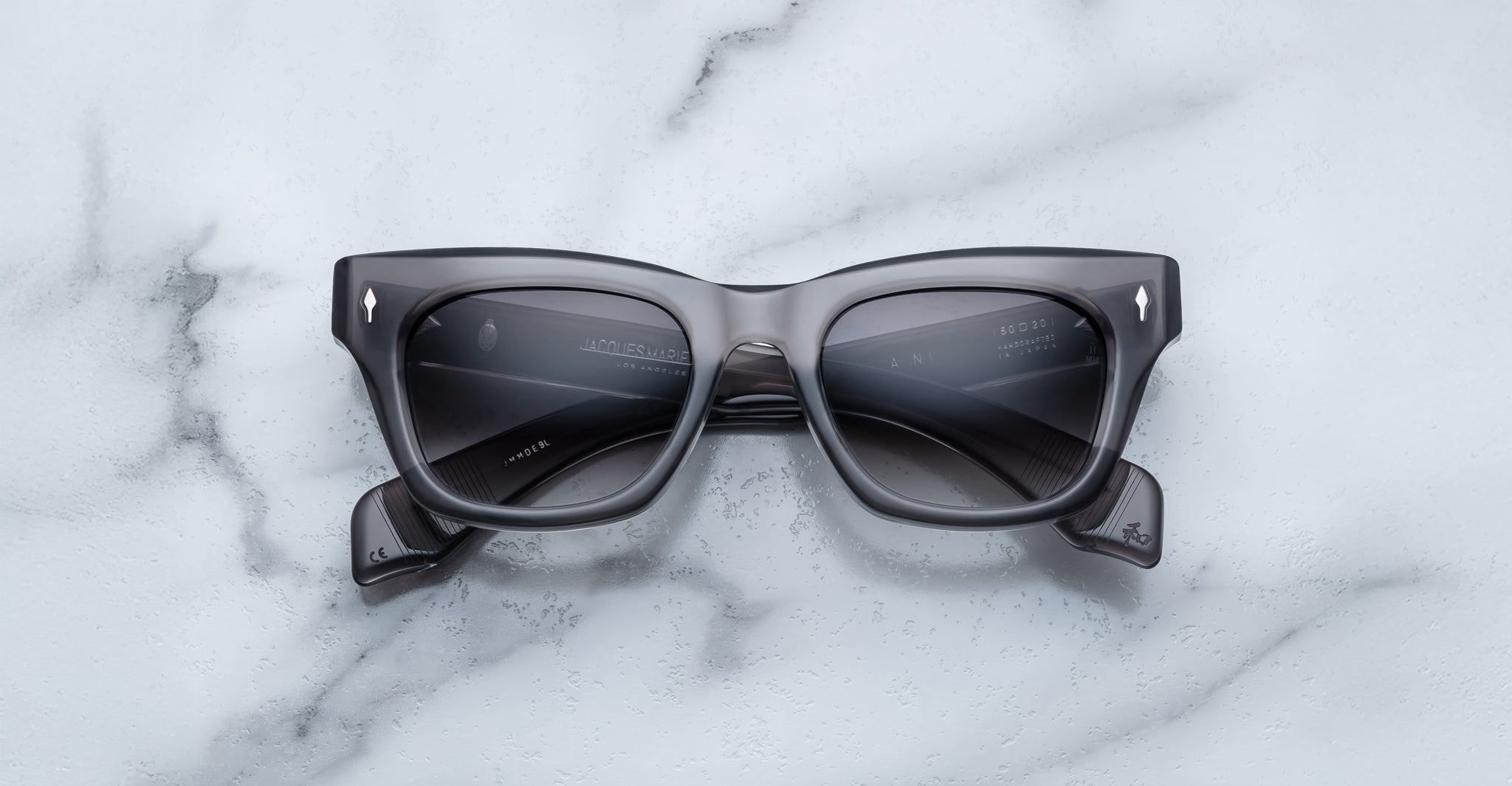 The Jacques Marie Mage Dealan 53 is a pair of black rectangular sunglasses with thick frames, shown face up on a white marble surface with folded arms.