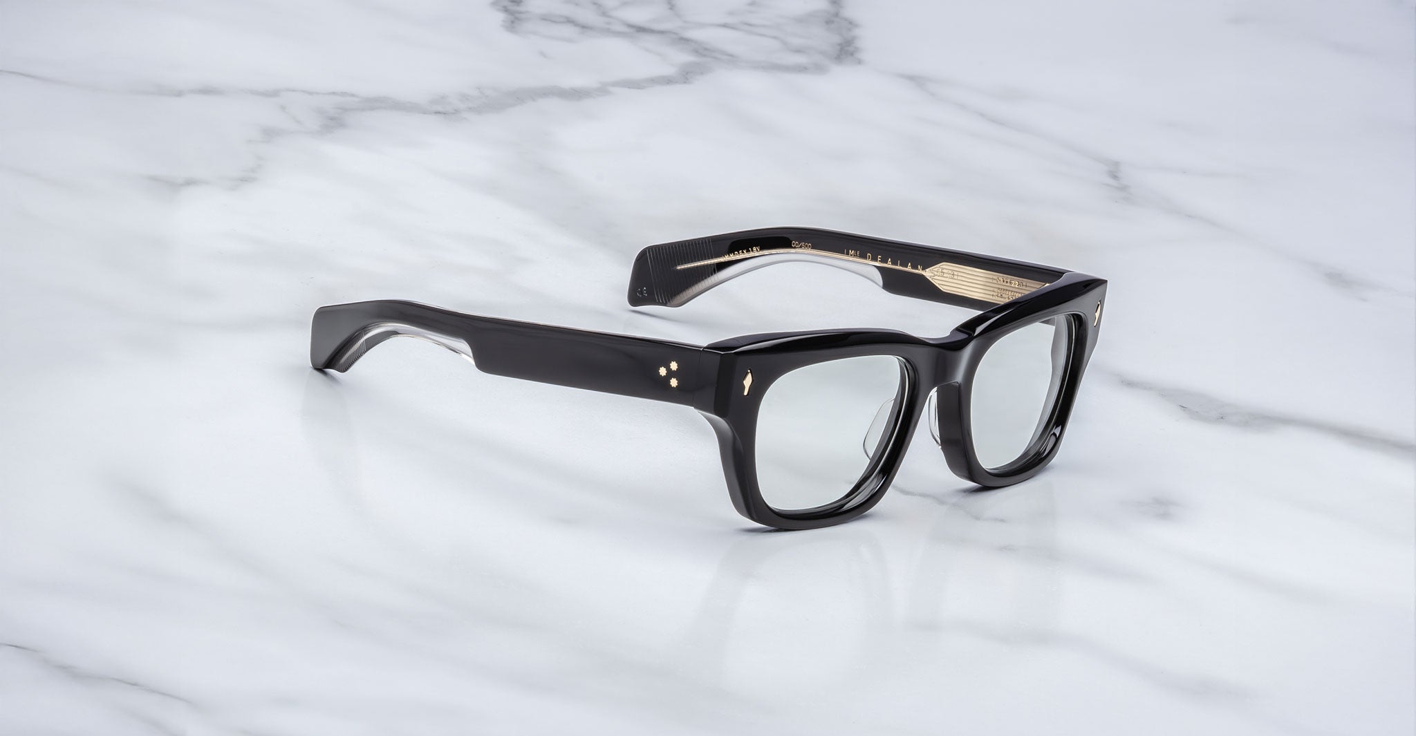The Jacques Marie Mage Dealan 53, a pair of black rectangular eyeglasses with thick frames and clear lenses, is displayed on a white marble surface.